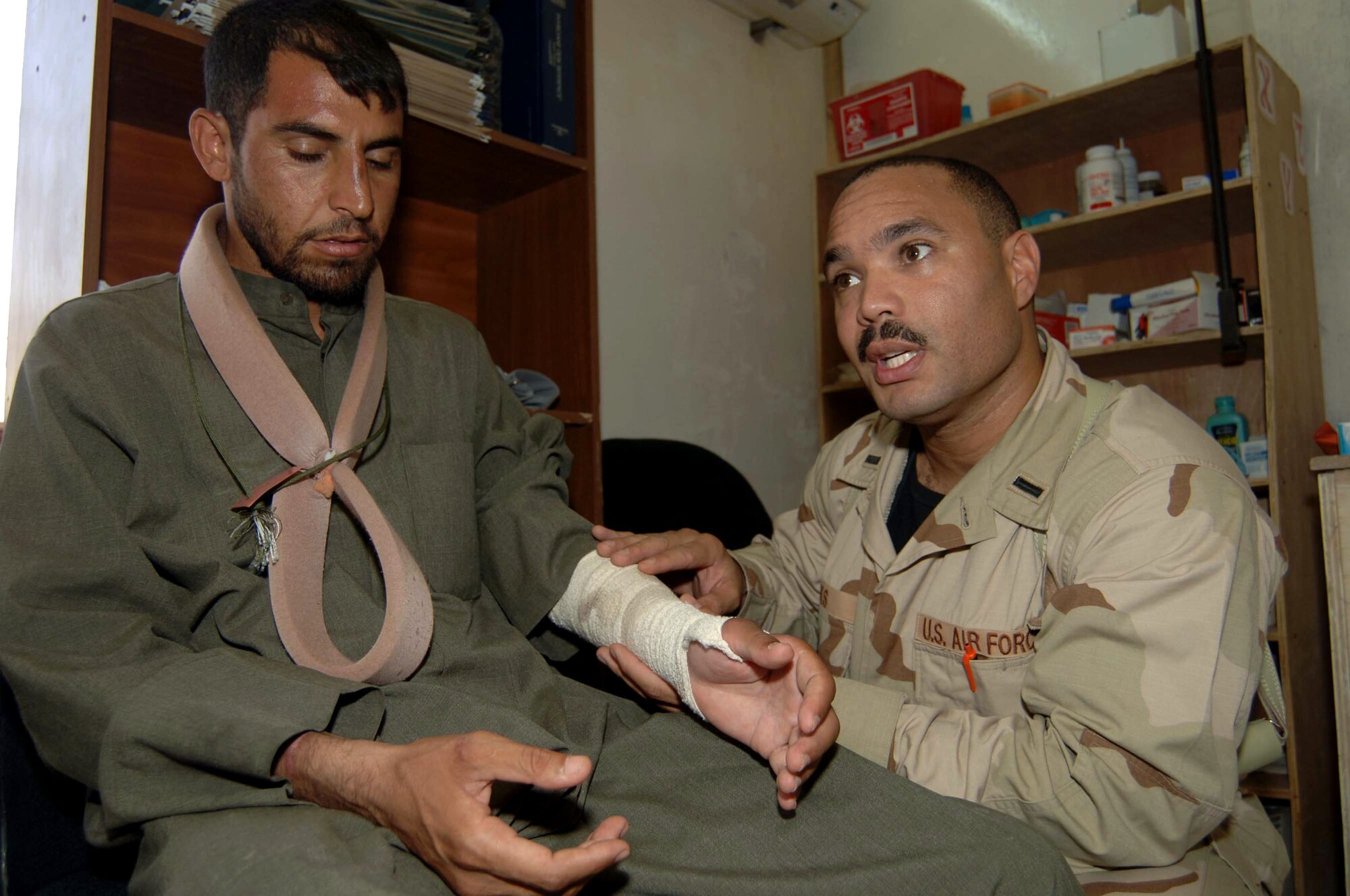 1st Lt. Robert Cooks speaks to an Arabic/English translator about an Iraqi patient's broken arm June 21 at Camp Striker, Iraq. Lieutenant Cooks is a 447th Expeditionary Medical Squadron medic and volunteers his free time to assist the Army at the Civil-Military Operations Center medical clinic here. The clinic provides free medical service to impoverished Iraqi citizens. (U.S. Air Force photo/Tech. Sgt. Russell Wicke) 
