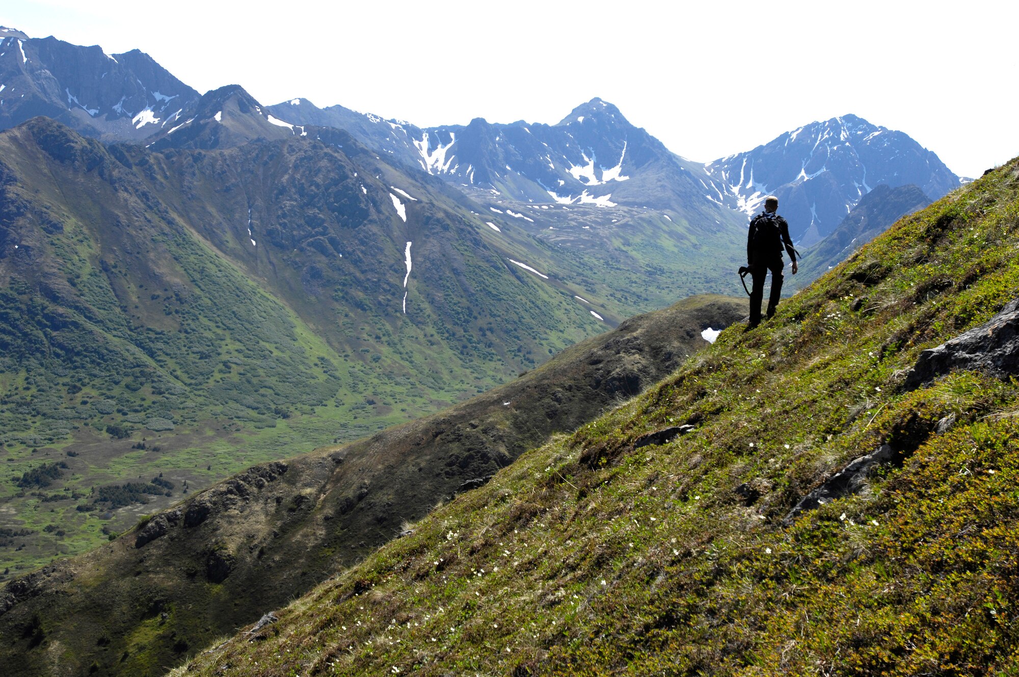 CHUGACH MOUNTAINS, Alaska -- 1st Lt. Luke Buckley hikes the rough terrain back to the drop off point after retrieving a tracking collar from a bear den that was designed to fall off during winter hibernation. Lieutenant Buckley is a Military Conservation Agents at Elmendorf Air Force Base, Alaska. He volunteered to help Alaska Department of Fish and Game biologists retrieve the collars. The bear tracking study, conducted by the ADFG, was funded by the Department of Defense to monitor the movements of brown bears on Elmendorf and neighboring Fort Richardson. On June 28, three teams of three agents were flown into the mountains with radio trackers and located the collars in the dens. (RELEASED) U.S. Air Force photo by Tech. Sgt. Keith Brown