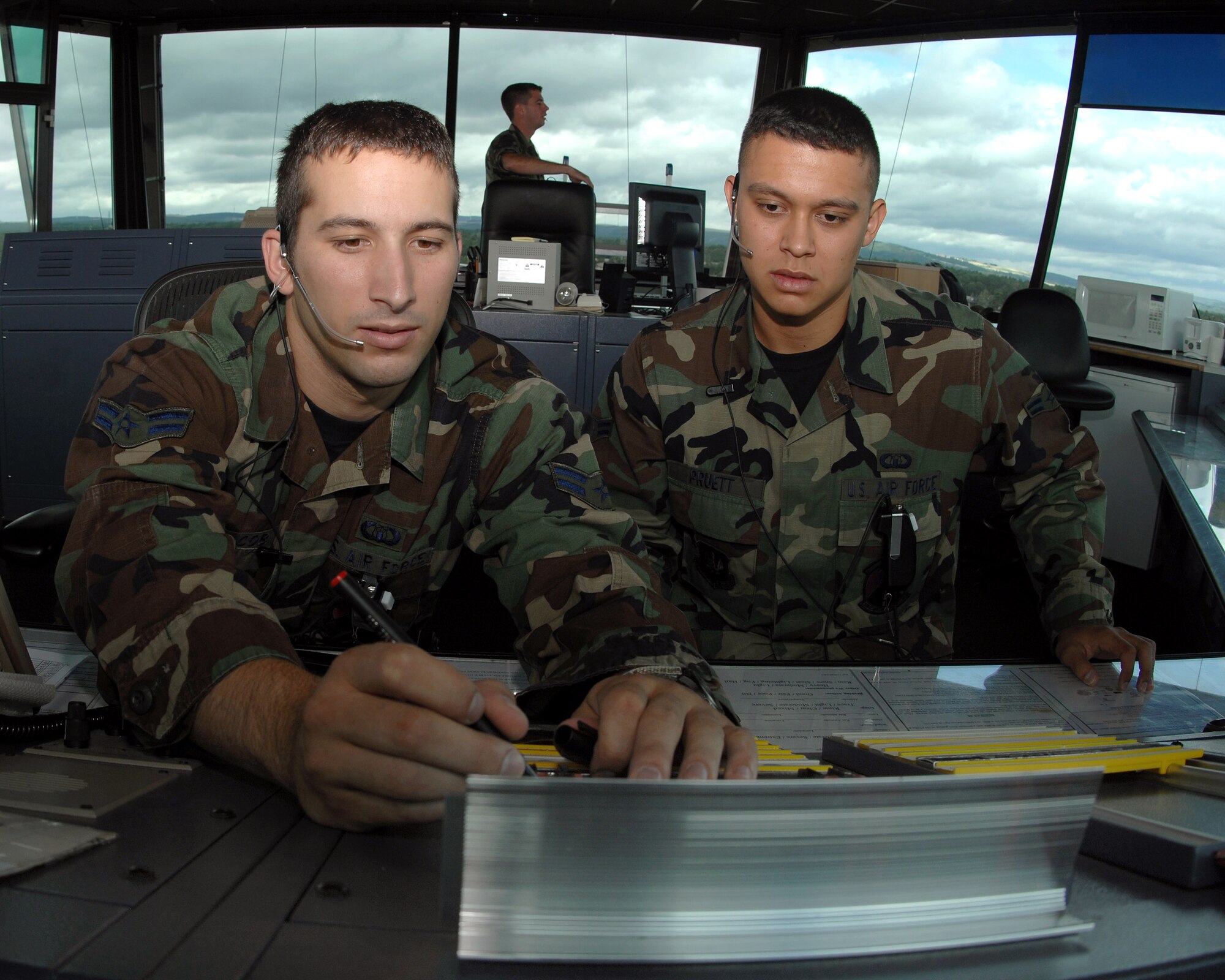 Airman 1st Class Toby Jacob (left) writes coordinates of an inbound aircraft on a flight progress strip while Airman 1st Class Earl Pruett talks to the pilot over the radio using a radio ear piece June 26 in the control tower at Ramstein Air Base, Germany. The Airmen are assigned to the 86th Operations Support Squadron. (U.S. Air Force photo/Airman 1st Class Kenny Holston)
