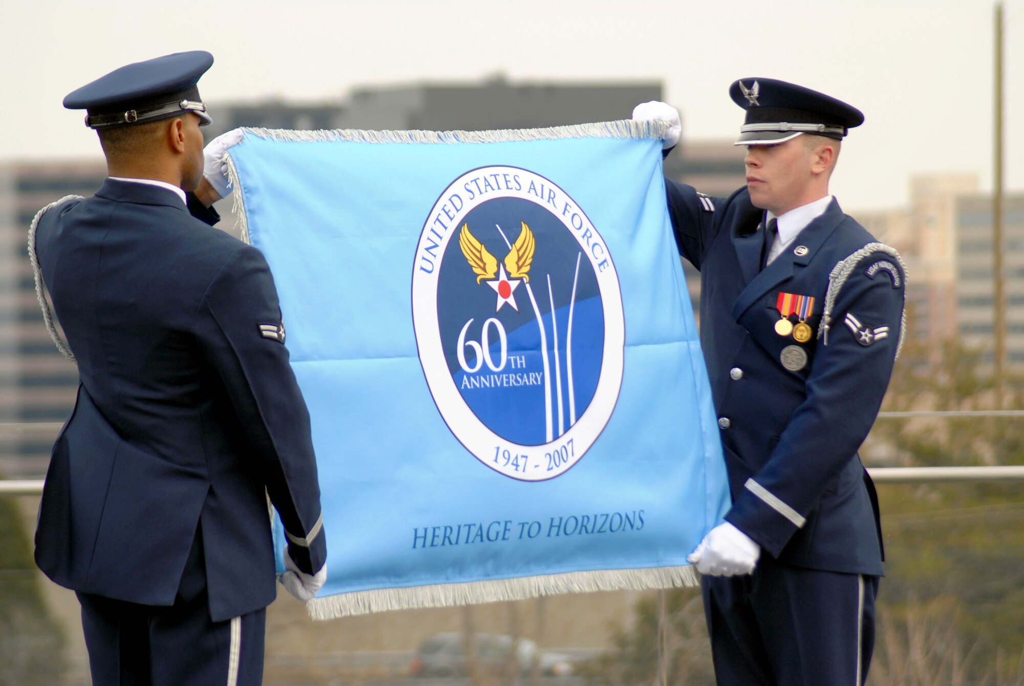 Airmen 1st Class Ahmad Ware (left) and Brandon Bridges unveil the Air Force 60th Anniversary flag for the first time March 1 at the Air Force Memorial in Arlington, Va.  The ceremony was attended by Chief of Staff of the Air Force Gen. T. Michael Moseley and Secretary of the Air Force Michael W. Wynn.   The Airmen are Air Force Honor Guard ceremonial guardsmen.  (U.S. Air Force photo/SSgt. Madelyn Waychoff)