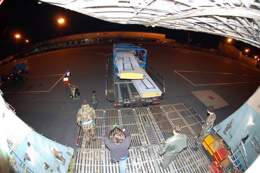 DOVER AIR FORCE BASE, Del. -- Mr. Donald Krauss (center), 436th Aerial Port Squadron ramp specialist, guides a K-loader into position as Staff Sgt. Ozvardo Taylor (left), 436th APS ramp services team chief, Master Sgt. Robin Morris (right), 89th Airlift Squadron loadmaster wait to upload two C-130 wings onto a C-5 Galaxy. The wings are part of an international effort organized to airlift two sets of C-130 wings purchased by the Royal Air Force from the Royal Australian Air Force to refurbish two aging C-130 in the UK. (U.S. Air Force photo/Tech. Sgt. Kevin Wallace)
