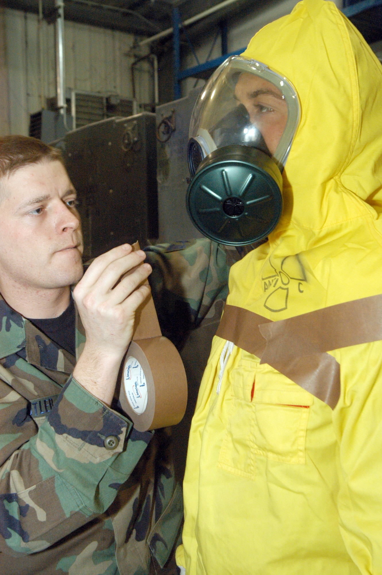 Senior Airman Chris Butler, a Readiness Flight readiness logistics journeyman, tapes loose edges of an anti-C (radiation suit) worn by Senior Airman Nick Pompa to minimize skin exposure. U.S. Air Force photo by Sue Sapp. 
