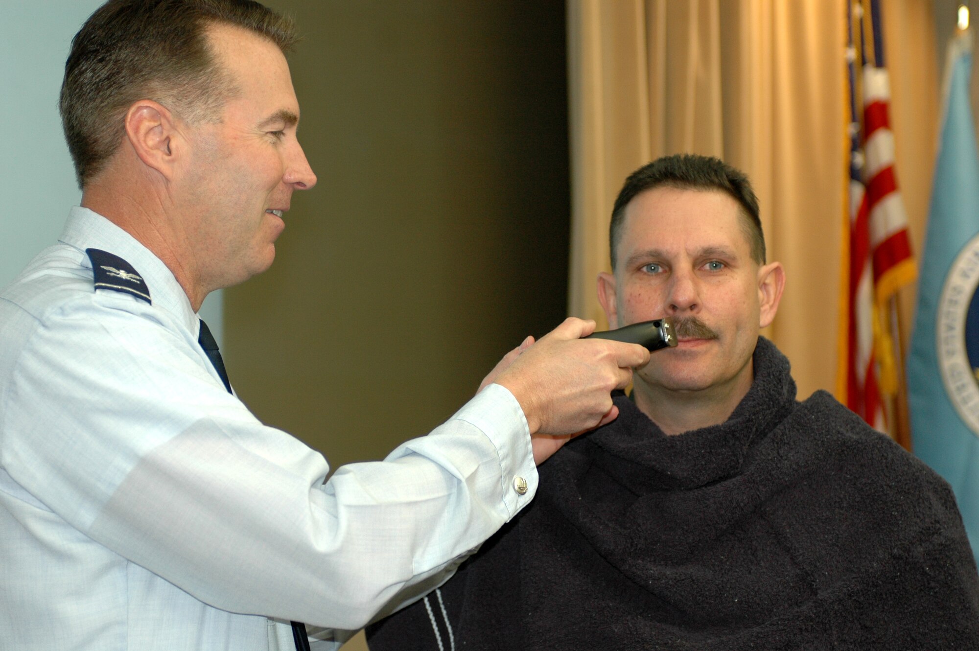 Col. Steve Arquiette, 60th Air Mobility Wing commander, shaves off Senior Master Sgt. William Griesemer, 22nd Airlift Squadron flight engineer superintendent’s mustache during wing standup Feb. 28. Sergeant Griesemer agreed to have his mustache shaved as part of  “Mustache March Madness.” “Mustache March Madness” is a fundraiser by the 22nd  Airlift Squadron to help raise funds for the Air Force Assistance Fund campaign. (U.S. Air Force photo by Staff Sgt. Candy Knight)