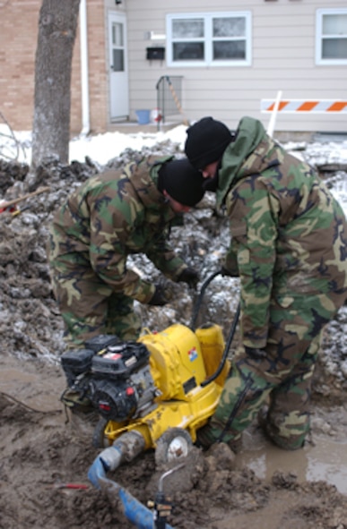 GRAND FORKS AIR FORCE BASE, N.D. -- Airman Tyler Peterson and Airman 1st Class Christopher Dunn, 319th Civil Engineer Squadron, prime a pump March 6 to clear water from an excavation to repair a broken water main here.  The broken water main was discovered March 5, leaving about 280 base housing residents temporarily without water.  The main was repaired March 7 and super-chlorinated as a safety precaution. (U.S. Air Force photo/Senior Airman J. Paul Croxon)