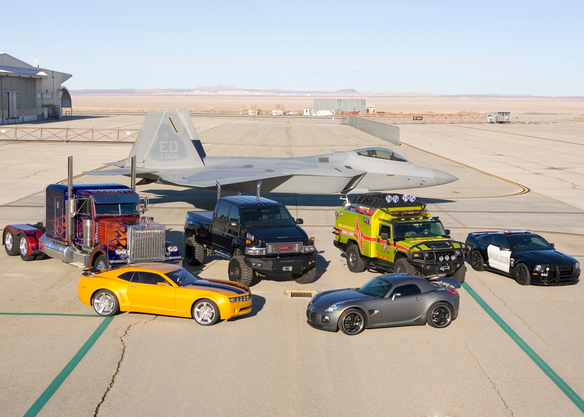 Several "Transformers" line up in front of an F-22A Raptor here Feb. 28, 2007. The vehicles were on base to shoot several scenes for the upcoming "Transformers" film.  The movie marks the first time non-computer-generated Raptors are depicted in a film. (Photo by Andy Wolfe)