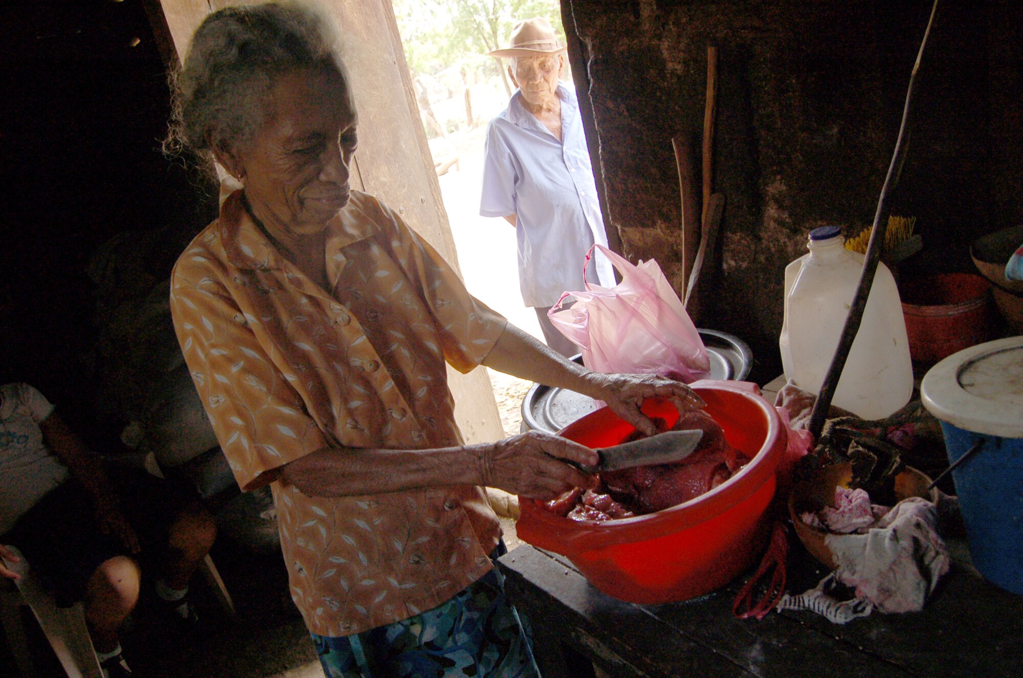 Luisa Palacio-Cortez slices beef on one of two tables in her two-room grey brick and wooden house as her husband, Selmo, watches through the doorway. The 83-year-old woman and her household of four survive off of about $11 to about $27 a month. (U.S. Air Force photo/Senior Airman Jacque Lickteig)