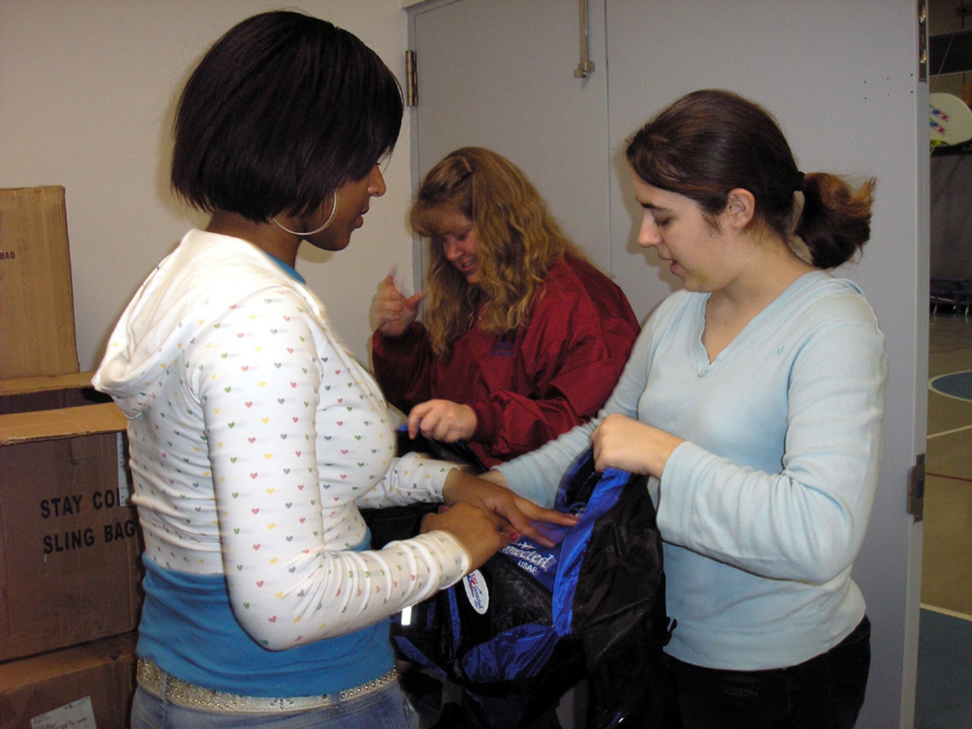 Amber Johnson, left, and Amanda Skrok, right, along with Youth Programs Director Cind Berg, put completed bags into boxes for storage. The 'Stay Connect' backpacks are available to any Malmstrom childe with a deployed or deploying parent.
