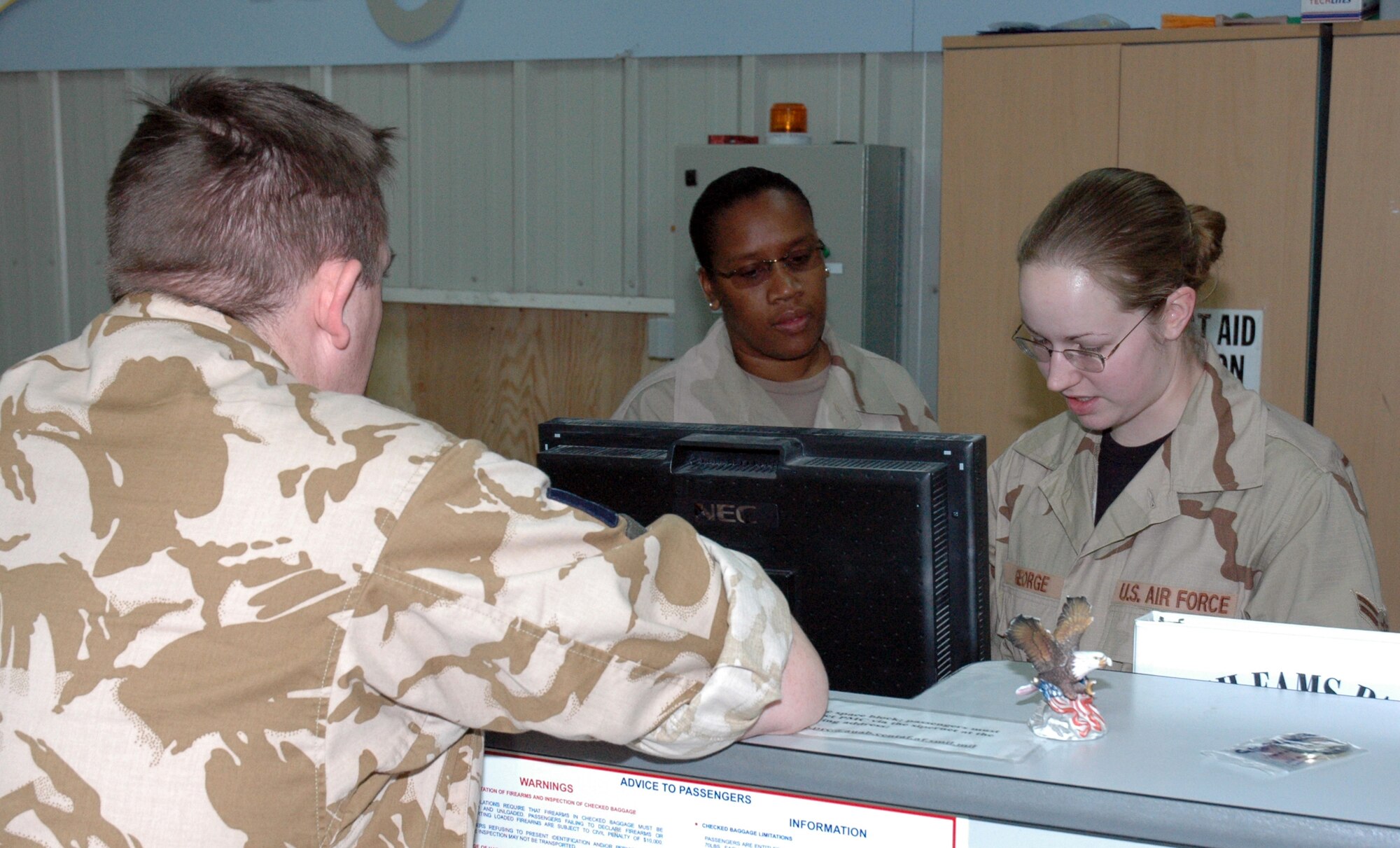 Tech. Sgt. Juliet Diggs (background) and Airman 1st Class Laura George (right), 8th EAMS passenger service agents, work with a member of the British Royal Air Force to process him for intratheater airlift. The squadron processed approximately 257,000 servicemembers, Coalition partners and federal contractors for travel in 2006. (U.S. Air Force photo by Senior Airman Erik Hofmeyer)