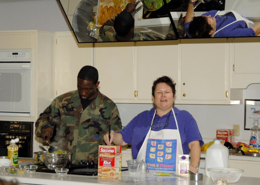 Rita Miller, Health and Wellness Center dietitian, explains the benefits of whole grains to an audience, while Senior Airman Antonio Jackson, HAWC diet technician, stirs a boiling pot of vegetables. The food demonstration is just one of the many classes the HAWC is holding to promote National Nutrition Month. The center will host a Commissary tour 9 - 10:30 a.m. March 15 to show a healthier way to shop for food. Participants will meet in the produce area. For more information or to join the Commissary tour, call 283-3826.  