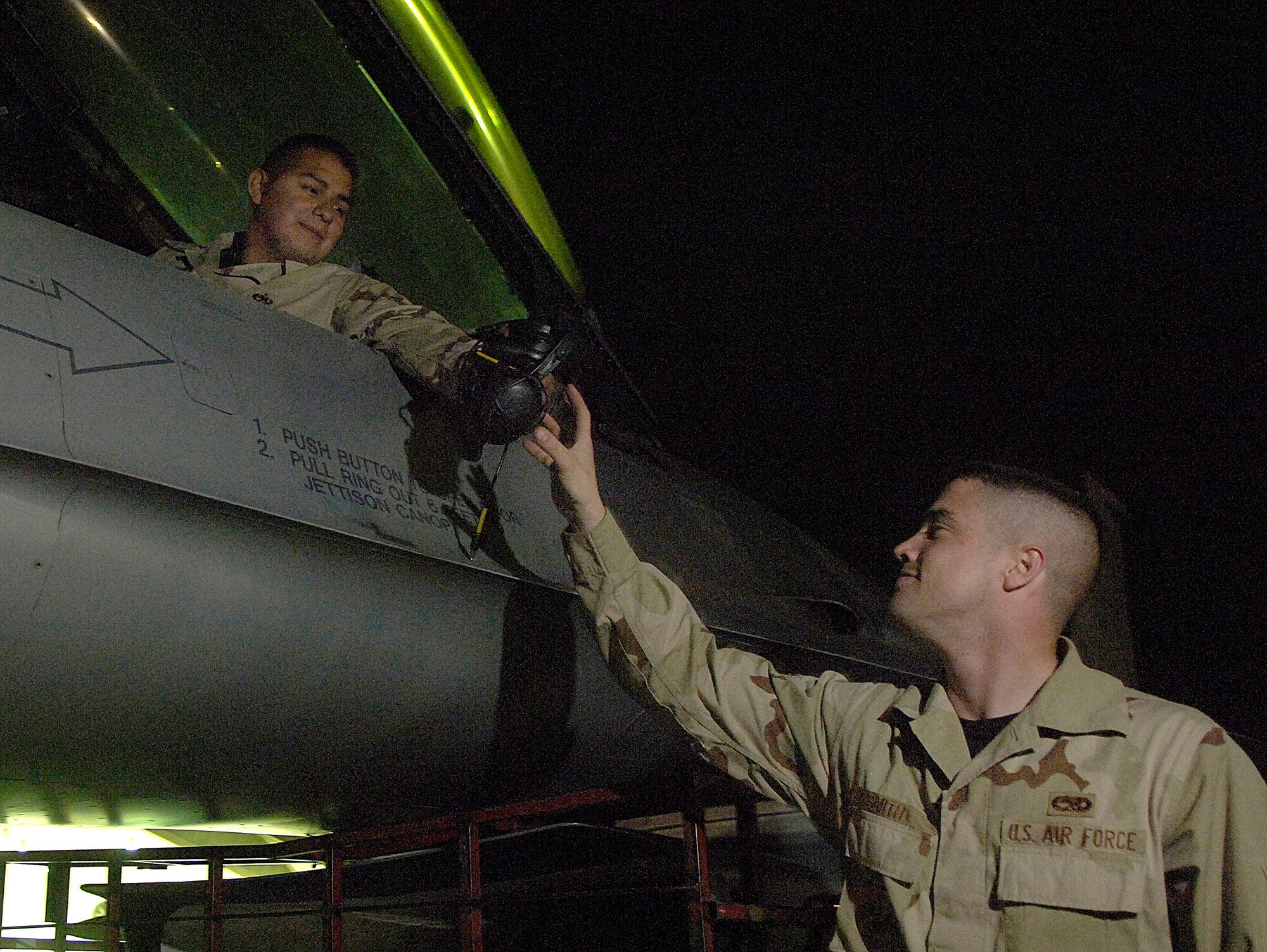 Staff Sgt. Jose Vuittonet hands hearing protection to Airman 1st Class Bruce Smith before completing engine run up checklists on an F-16 Fighting Falcon March 4 at Balad Air Base, Iraq. The Airmen are assigned to the 332nd Expeditionary Aircraft Maintenance Squadron. (U.S. Air Force photo/Airman 1st Class Nathan Doza) 