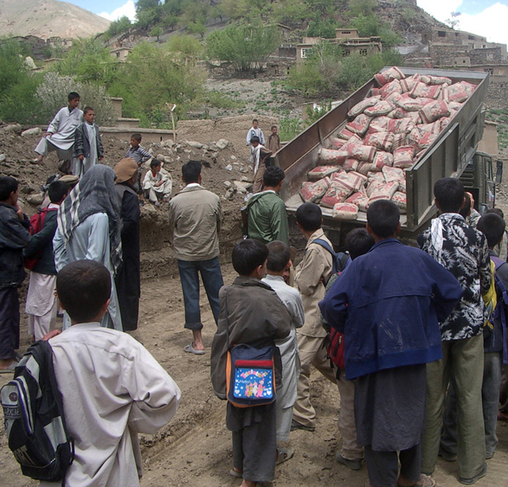 Afghanistan villagers in the Khenj district watch as bags of ready-to-mix cement are unloaded in Panjshir Province, Afghanistan. The cement was used to repair a retaining wall that protects a mosque. (U.S. Air Force photo/Capt. Chris White)
