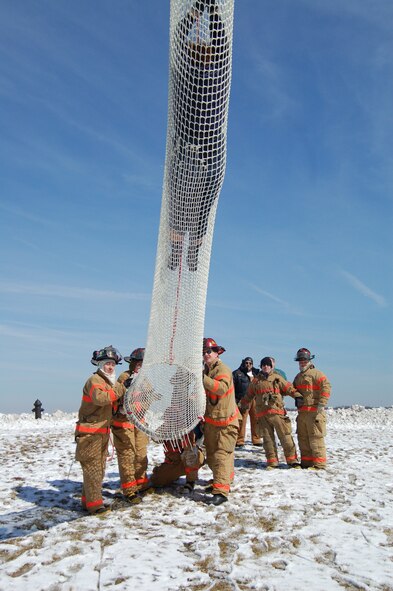 A tower controller slides down the Baker Life Chute as 436th Civil Engineer Squadron firefighters (left to right) Airman Kyle Herron, Airman 1st Class Darliska Blessing, Jeffrey McCombs and Tom Peers wait help her safely exit from the chute. (U.S. Air Force photo by Tech. Sgt. Kevin Wallace)