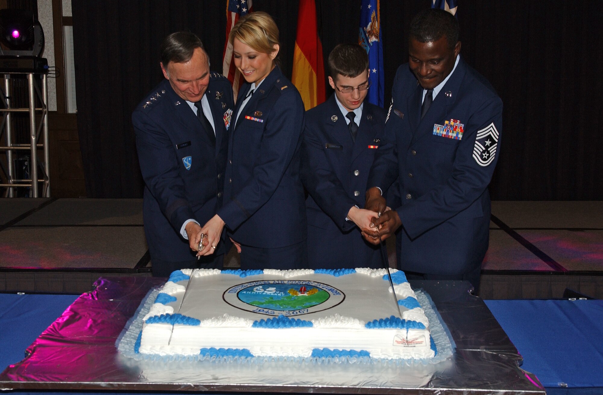 The two most junior ranking Airmen in attendance assist Gen. Tom Hobbins (left), Commander U.S. Air Forces in Europe, and Chief Master Sgt. Gary Coleman (right), USAFE Command Chief Master Sergeant, in slicing a cake at the USAFE 65th Anniversary Dinner Concert celebrated March 10 at the Ramstein Officers’ Club. In keeping with tradition, the most junior officer and enlisted Airmen participated in the cake cutting ceremony. On Saturday, the honors went to 2nd Lt. Amanda DeLancey, a contracting officer from the 52nd Contracting Squadron at Spangdahlem Air Base, Germany, and to Airman Basic James Summerer, a command post controller with the 603rd Air Operations Center at Ramstein. Photo by Senior Airman Erin Peterson.
