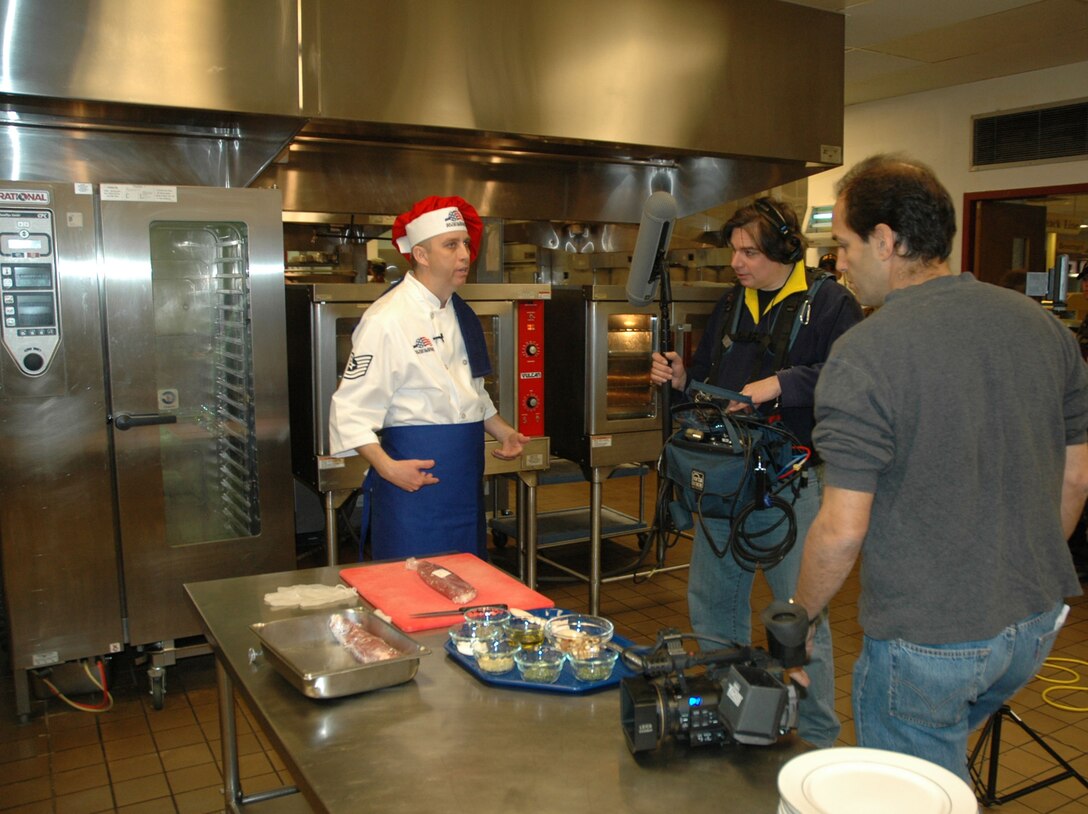 Alan Madison, Emeril Live producer, and sound technician Gary Tole prepare to begin taping Tech. Sgt. Wesley Williams preparing his award winning rainbow fruit stuffed pork tenderloin. Mr. Madison and Mr. Tole were among the Emeril Live production team visiting Ellsworth March 13 to film Sergeant Williams in his kitchen. Sergeant Williams will visit the Emeril Live show April 6 and the episode is scheduled to air sometime in June.