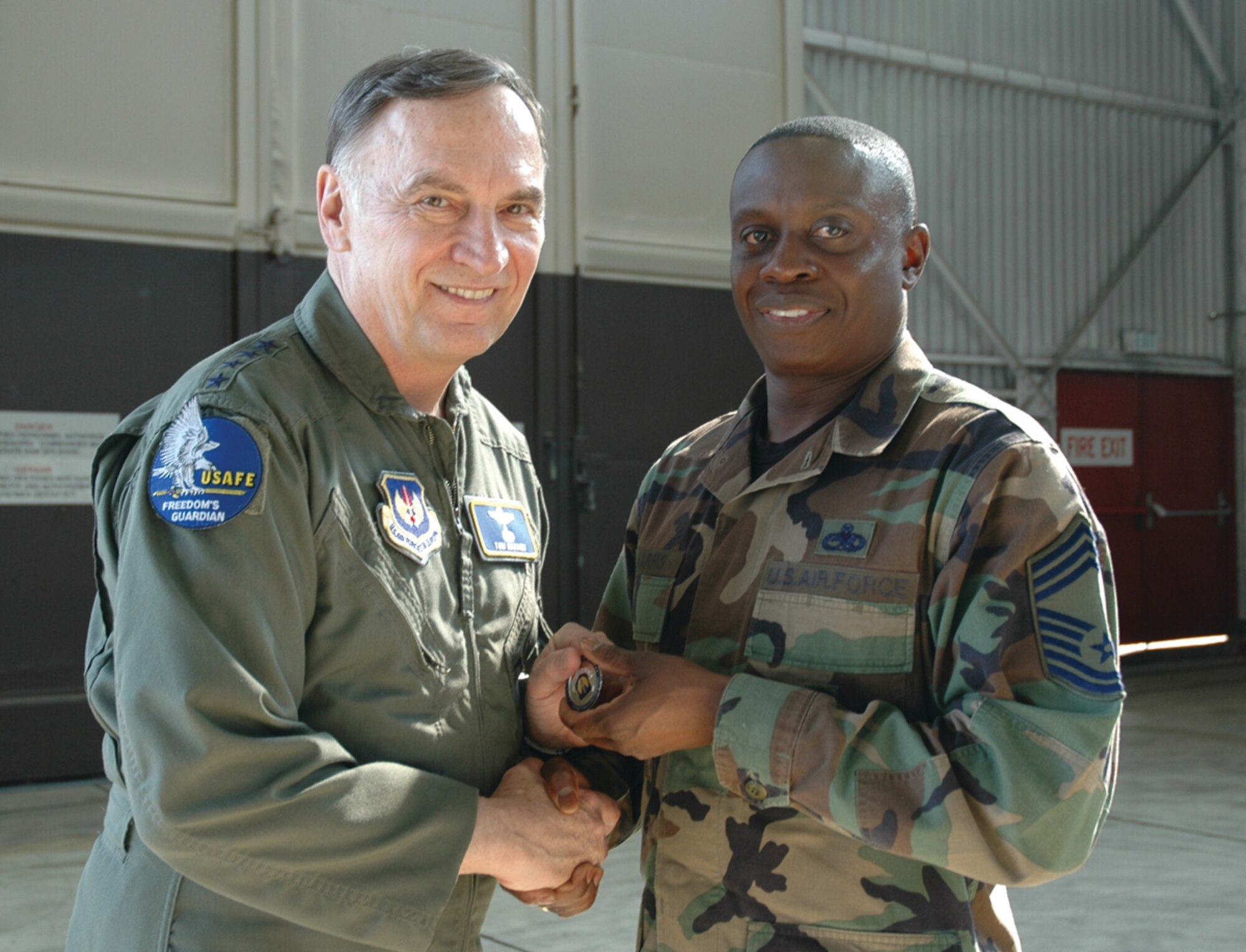 SPANGDAHLEM AIR BASE, Germany -- Gen. Tom Hobbins, U.S. Air Forces in Europe commander, coins Chief Master Sgt. Maurice Harris, 52nd Maintenance Group, while at Spangdahlem Air Base to shoot an American Forces Network commercial here March 15.  