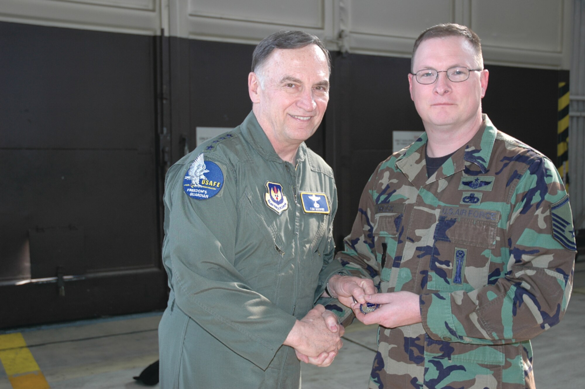 SPANGDAHLEM AIR BASE, Germany -- Gen. Tom Hobbins, U.S. Air Forces in Europe commander, coins Master Sgt. Charles Shock, 52nd Maintenance Group, while at Spangdahlem Air Base to shoot an American Forces Network commercial here March 15.