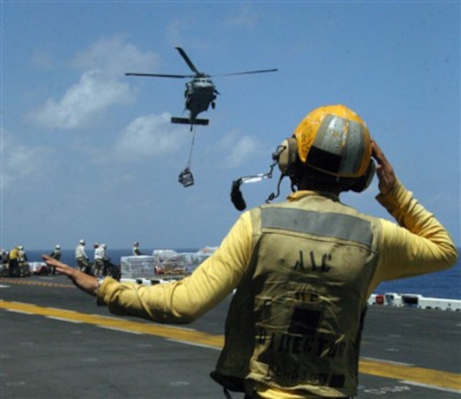 A U.S. Navy aviation boatswain's mate handler guides an MH-60S Nighthawk helicopter into position to release a pallet of cargo onto the flight deck of the amphibious assault ship USS Bataan (LHD 5) on March 16, 2007, during a vertical replenishment operation with the Military Sealift Command combat stores ship USNS Concord (T-AFS 5).  The Bataan is supporting maritime security operations in the U.S. Naval Forces Central Command area of operations.  