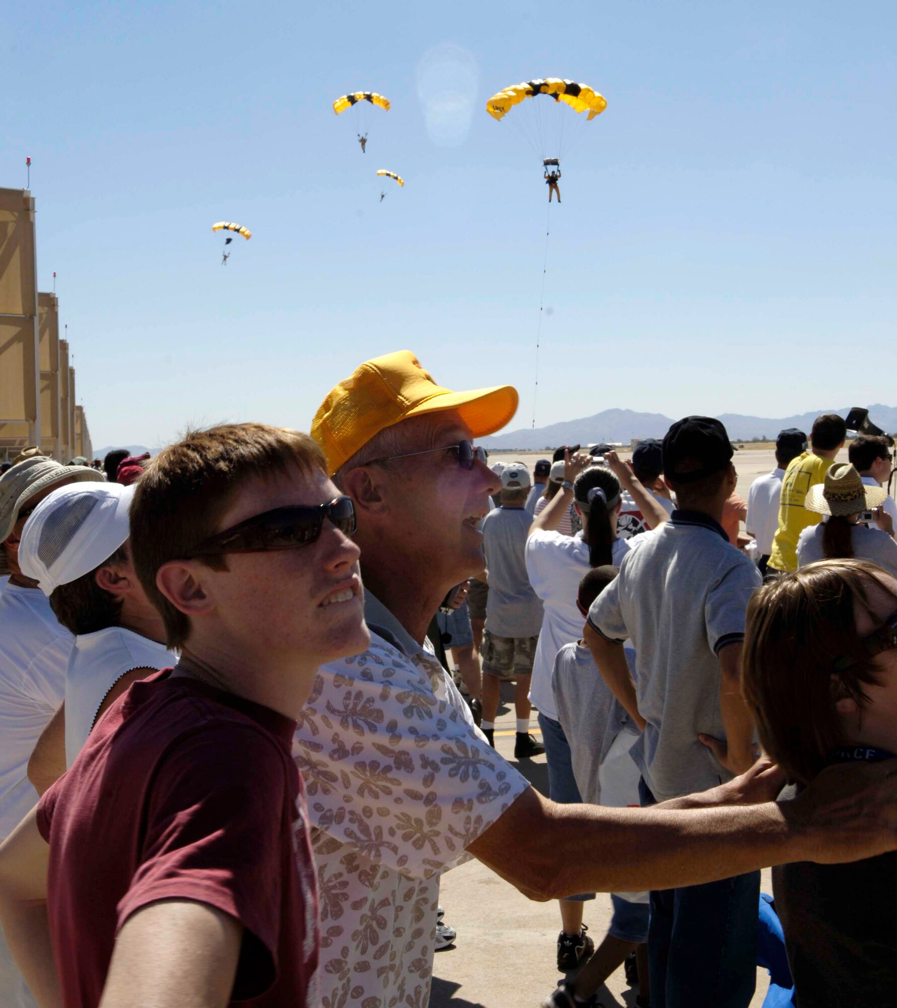Spectators look on as the Golden Knights U.S. Army parachute team glides over the crowd March 18 during the 2007 Aerospace and Arizona Days air show at Davis-Monthan Air Force Base, Ariz.  The two-day air show offered public an up-close look at military and civilian aerial demonstrations and static-display aircraft from across the U.S. The theme for this year's show was "Davis-Monthan and Tucson: 80 Years of Airpower for America!" (U.S. Air Force photo/Senior Airman Jesse M. Shipps)