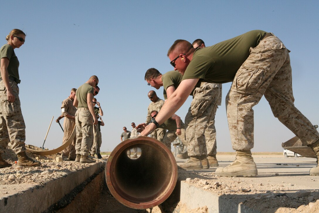 AL ASAD, Iraq- Marines from Marine Wing Support Squadron 271 engineer section roll a 14-inch-pipe into a four foot trench on the flight line, Mar., 23.  The pipe will house a fuel line and be covered with cement.