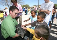 Animal Encounter team member Jason Baca holds Ginobili, a giant Tegu lizard, while Team Lackland children pet the reptile. Ginobili rides in a safety-approved kennel while traveling in the SeaWorld and Busch Gardens Animal Adventures Tour Vehicle. The 38-foot tour vehicle, with its various reptiles and birds, was on base March 15 to give Team Lackland a chance to meet and interact with the animals. The Animal Adventures Tour Vehicle will visit more than 20 of the nation's largest cities during the tour year. (USAF photo by Robbin Cresswell)