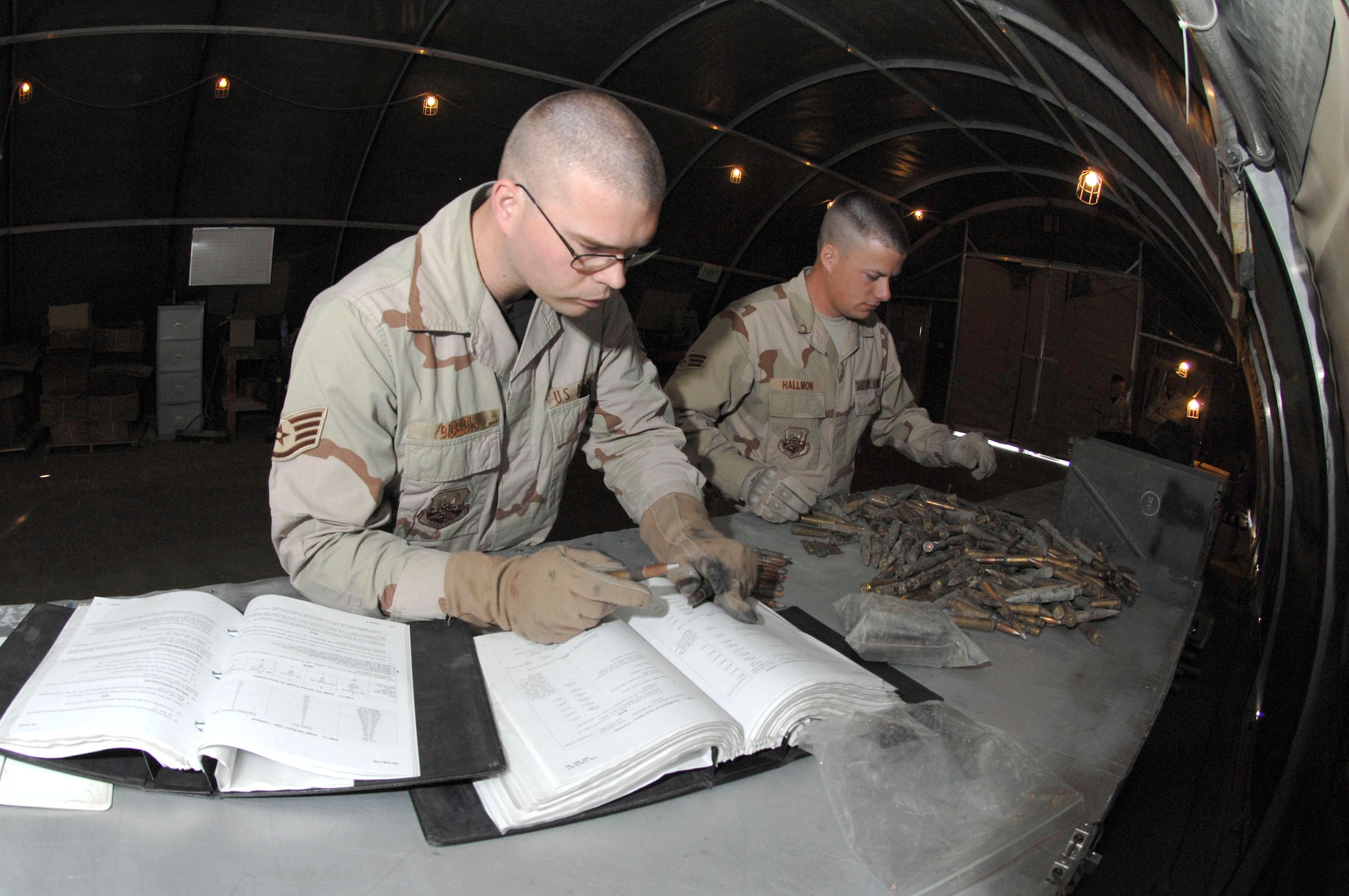 Staff Sgt. Michael Bigelow checks a technical order to determine what to watch for while inspecting certain types of munitions, while Senior Airman David Hallmon sorts unfired ammunition March 21 at Kirkuk Air Base, Iraq. All unserviceable ammo is sent to the explosive ordnance disposal team for detonation. The Airmen are munitions specialists with the 506th Air Expeditionary Group.  (U.S. Air Force photo/Senior Airman Bradley A. Lail)