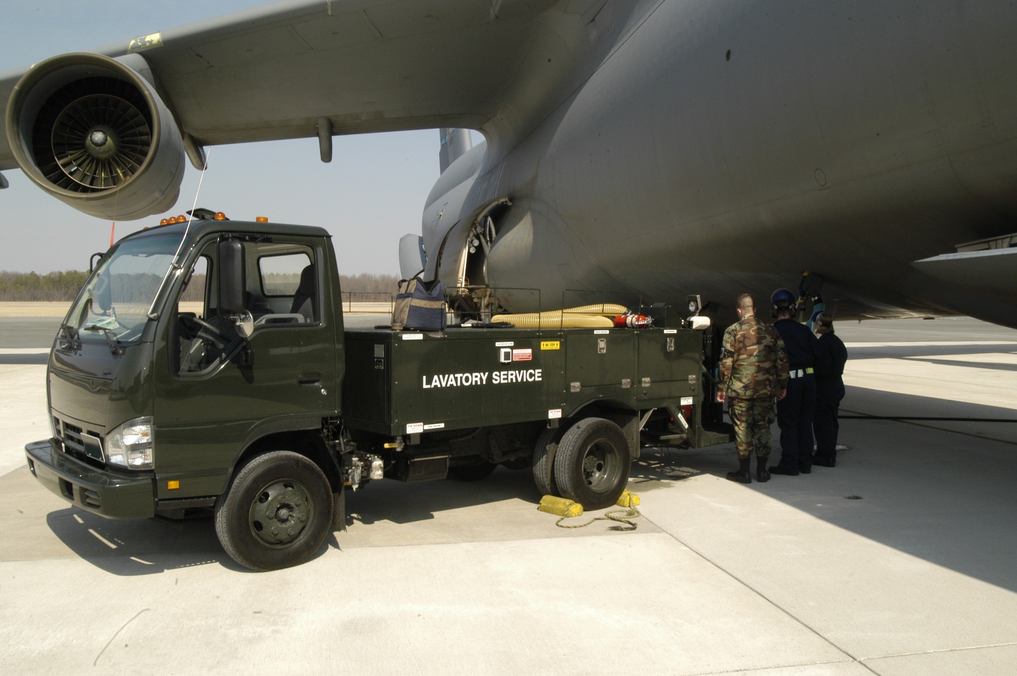 DOVER AIR FORCE BASE, Del. -- Fleet Services flight members prepare an aircraft here for departure by draining waste from the aircraft’s lavatories into one of the flight’s Latrine Servicing Trucks, as 2nd Lt. Eric Wicklund, Fleet Services Flight commander, looks on.  Flight members rotate working the clean side of Fleet – delivering meals, pillows and blankets – and working the dirtier side – cleaning the interior of the aircraft, removing trash, and cleaning and servicing the lavatories. (U.S. Air Force photo/Senior Airman James Bolinger)