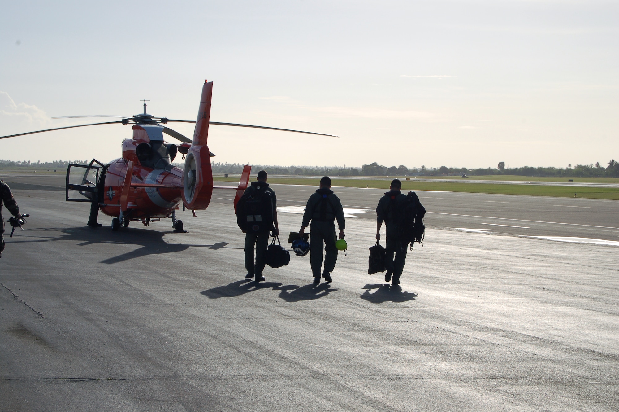 Coast Guard Lt. Cmdr. Juan Lopez (center) and two other Coast Guardsmen walk out to an HH-65C Dolphin March 21 at Coast Guard Air Station Borinquen, Puerto Rico. Their mission was to work with the Puerto Rican Police Department and help them train on how to dive out from a helicopter to rescue people at sea. A former Senior Airman, Commander Lopez is an aircraft commander and the assistant operations officer at the air station. Coast Guard Air Station Borinquen is based at what used to be Ramey Air Force Base, which closed in 1973. (U.S. Air Force photo/Tech. Sgt. Ben Gonzales)