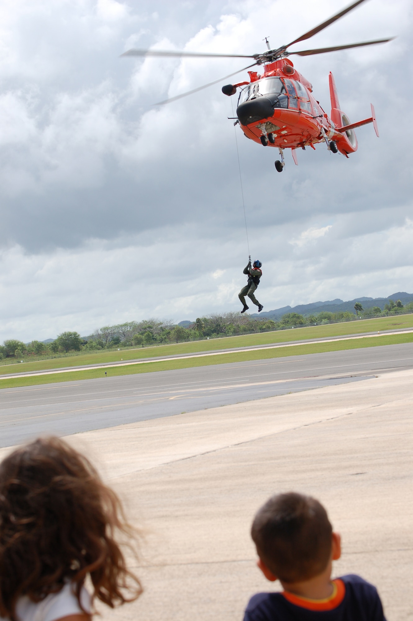 A Coast Guard HH-65C Dolphin crew demonstrates the helicopter's capability to hoist a person up into the helicopter during a March 22 open house at Coast Guard Air Station Borinquen, Puerto Rico. Approximately 500 visitors got a firsthand look at today's military members and equipment in Puerto Rico, and to see an historic C-54 cargo plane used during the Berlin Airlift. (U.S. Air Force photo/Tech. Sgt. Ben Gonzales)