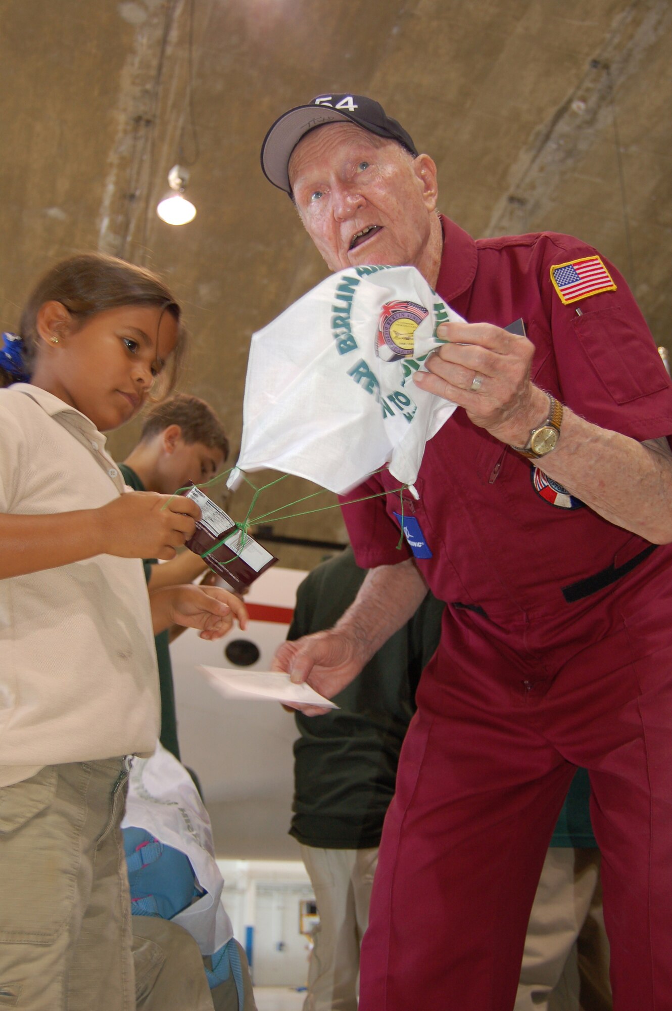 Adriana Tout learns how to tie candy to a handkerchief parachute from Retired Col. Gail Halvorsen March 22 during an open house at Coast Guard Air Station Borinquen, Puerto Rico. Colonel Halvorsen, also known as the Berlin Candy Bomber, flew C-54 Skymasters during the Berlin Airlift and parachuted candy to children from his airplane. Adriana, 8, is a Ramey School third grader. This was Colonel Halvorsen's first return to what was once Ramey Air Force Base since 1949, when he flew C-54 missions from Puerto Rico to South America. (U.S. Air Force photo/Tech. Sgt. Ben Gonzales)

