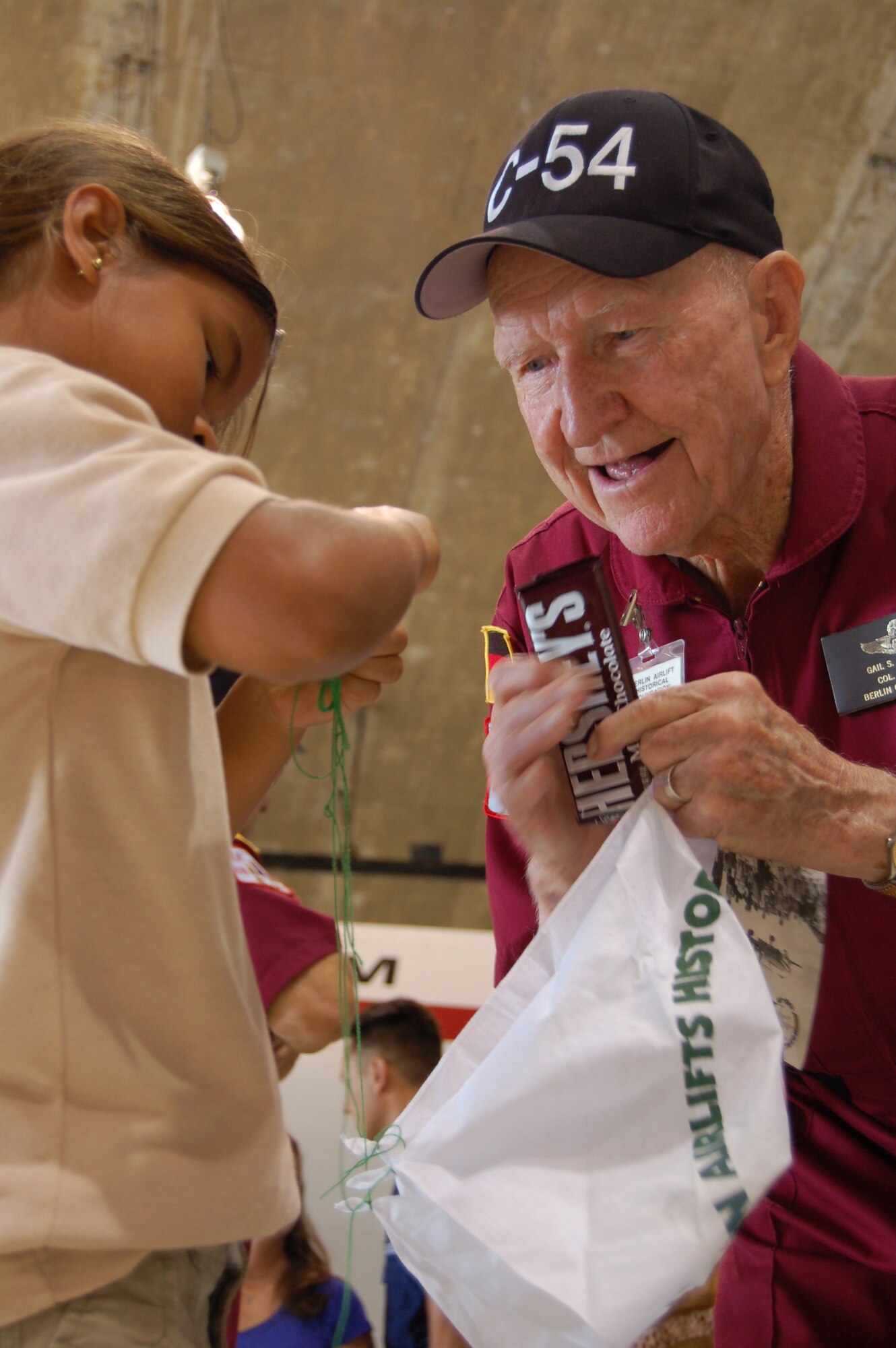 Adriana Tout learns how to tie candy to a handkerchief parachute from Retired Col. Gail Halvorsen March 22 during an open house at Coast Guard Air Station Borinquen, Puerto Rico. Colonel Halvorsen, also known as the Berlin Candy Bomber, flew C-54 Skymasters during the Berlin Airlift and parachuted candy to children from his airplane. Adriana, 8, is a Ramey School third grader. This was Colonel Halvorsen's first return to what was once Ramey Air Force Base since 1949, when he flew C-54 missions from Puerto Rico to South America. (U.S. Air Force photo/Tech. Sgt. Ben Gonzales)