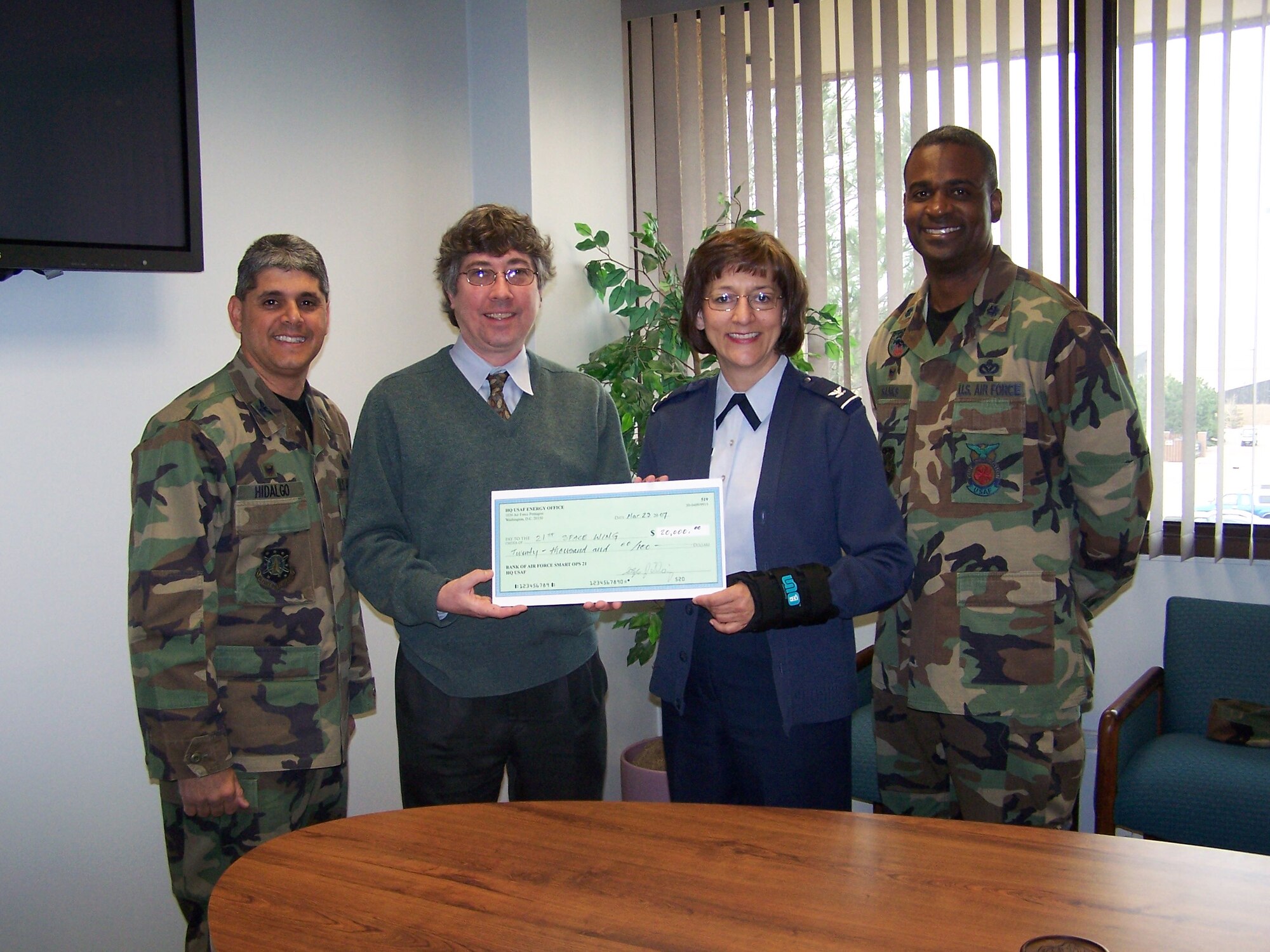 Mr. Stephen Doig, Air Force Smart Operations 21 highly qualified expert, presents a check for $20,000 to Col. Liz Anderson, individual mobilization augmentee to the 21st Space Wing commander, Col. Manuel Hidalgo, 21st Mission Support Group Commander (far left), and Lt. Col. Derrek Sanks, 21st Civil Engineer Squadron Commander (far right). The check was presented at the conclusion of a week long energy audit, aimed at finding low or no cost opportunities to make Peterson AFB more energy efficient.  The $20,000 will be used to fund some of the energy projects identified by the audit team.