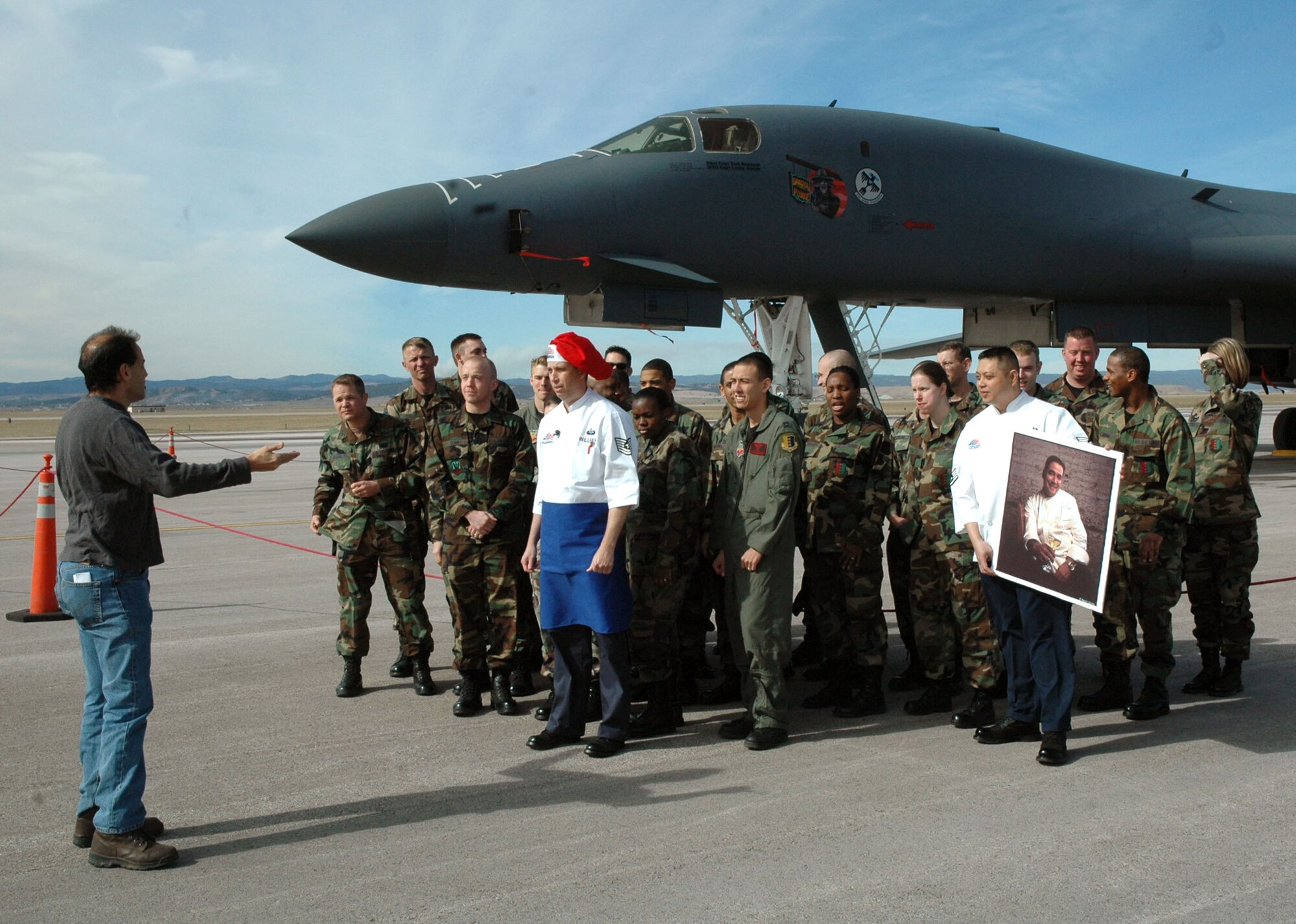 Alan Madison, 'Emeril Live' producer, directs a crowd of Ellsworth Air Force Base, S.D., Airmen in front of a B-1B Lancer to film an opening shot for the 'Emeril Live' show. On Mr. Madison's cue, Tech. Sgt. Wesley Williams, dining facility manager here and winner of the 'Emeril Live' military chef contest, challenged Emeril to successfully copy his recipe. After Sergeant Williams threw down the culinary gauntlet, the group of Airmen let out a resounding "Bam!" (U.S. Air Force photo/Tech. Sgt. Steven Wilson)