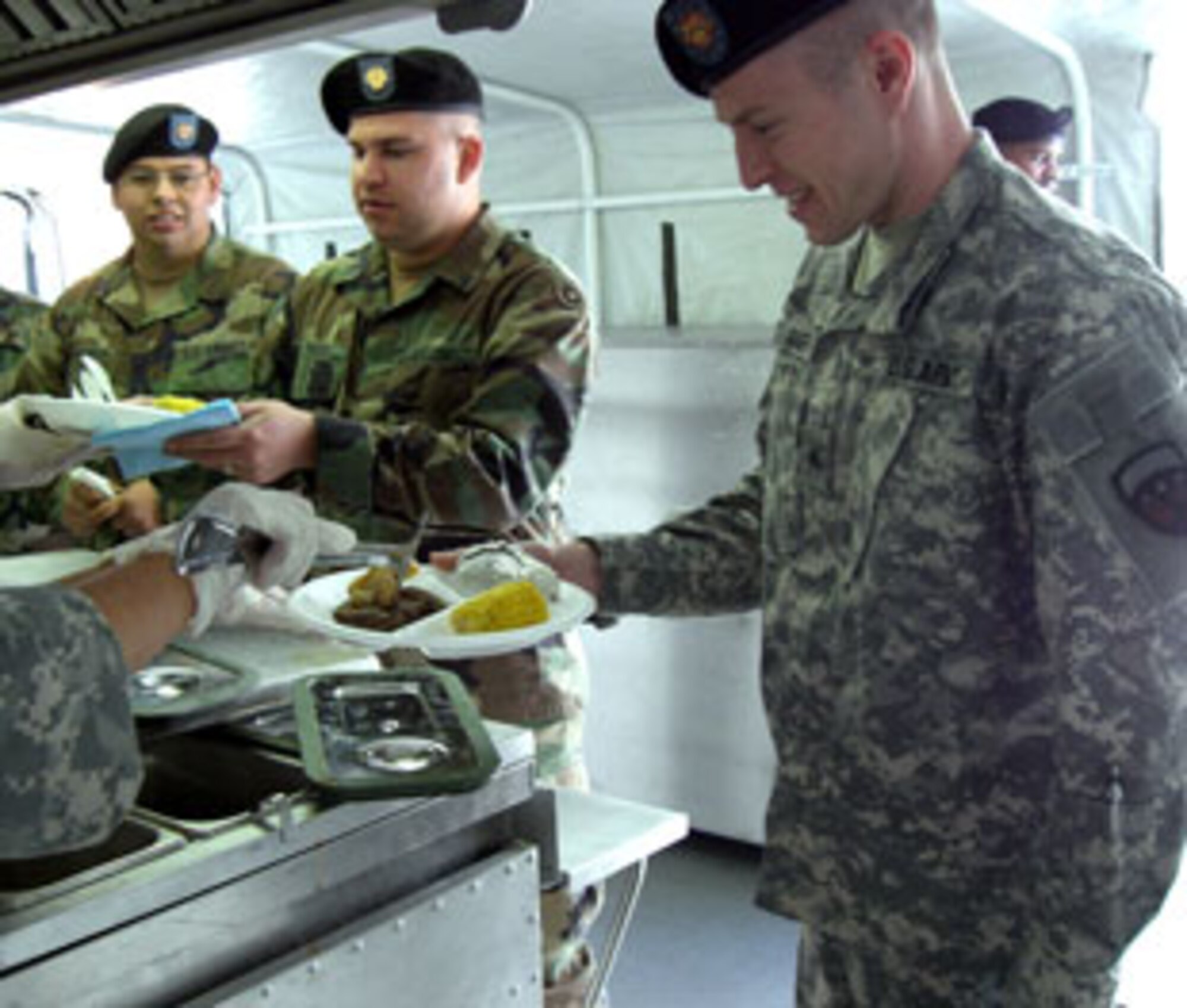 Spc. Raymond Menjiver, left, Spc. Joshua Fouch, and Sgt. Christopher Gimber, right, fill their plates with food from the 304th’s Mobile Kitchen.  Soldiers of the 304th Sustainment Brigade at March Air Reserve Base, Calif., were treated to a hot meal on the weekend as part of the debut of the unit's Containerized Kitchen, a trailer that has all of the equipment necessary for meal (U.S. Army photo by Spc. K. Christopher Witt)  