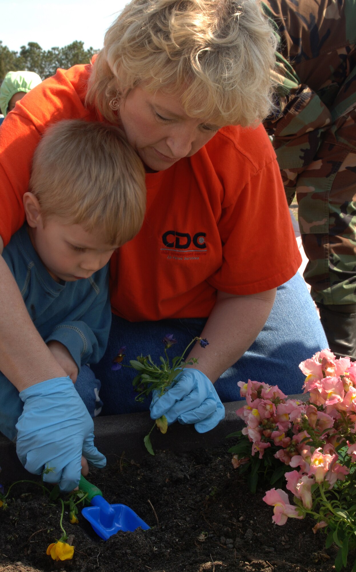 Sue Bonner, Russ Child Development Center childcare provider, helps three-year-old Aiden Slater, son of Staff Sgts. Michael and Misty Slater, plant flowers for spring at the CDC March 28. Children also planted vegetable gardens made of corn, carrots, strawberries and canteloupe. (U.S. Air Force photo/Senior Airman Michelle Arslan)