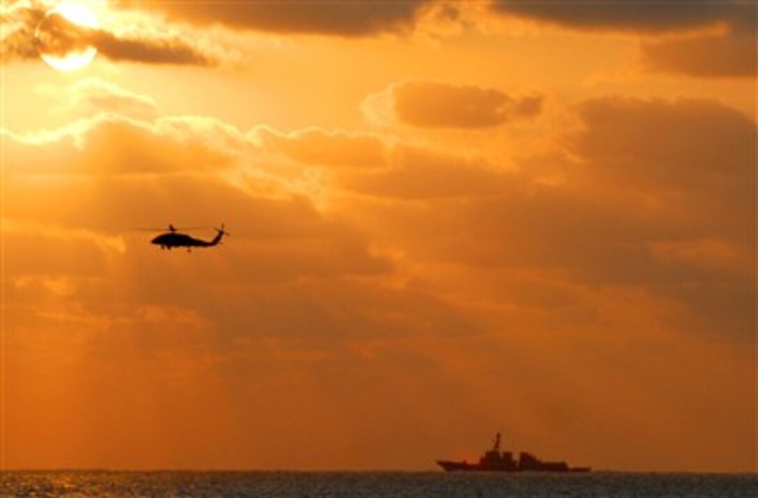 A destroyer steams along the starboard side of the Nimitz-class aircraft carrier USS Harry S. Truman March 22, 2007, as an SH-60 Seahawk helicopter assigned to Helicopter Squadron Seven conducts plane guard during flight operations over the Atlantic Ocean.