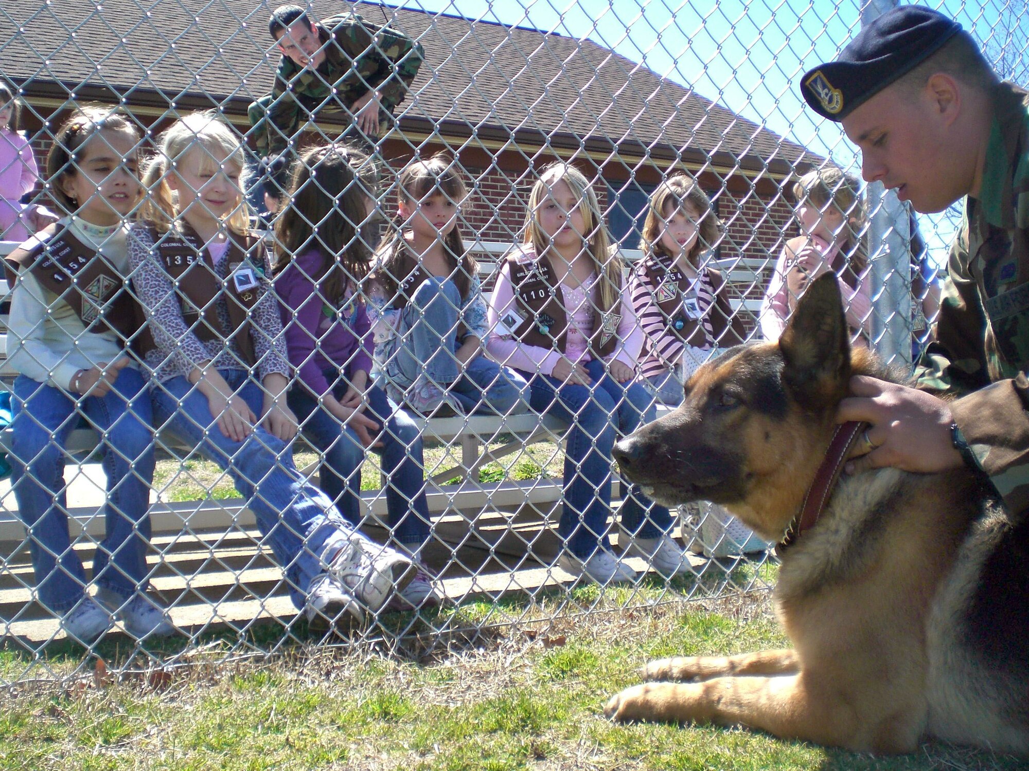 Girl Scout Troop 1354 from Poquoson watches as Senior Airman Shane Larson, 1st Security Forces Squadron, prepares military working dog Drak for a demonstration here March 30. The scouts showed their support for deployed troops by giving Hampton Roads families the opportunity to buy cookies for deployed Airmen. During the month-long cookie sale, the girls collected more than 60 boxes of cookies and presented them to the 1st Security Forces Squadron before the military working dog demonstration. (U.S. Air Force photo/Airman 1st Class Chase S. DeMayo)