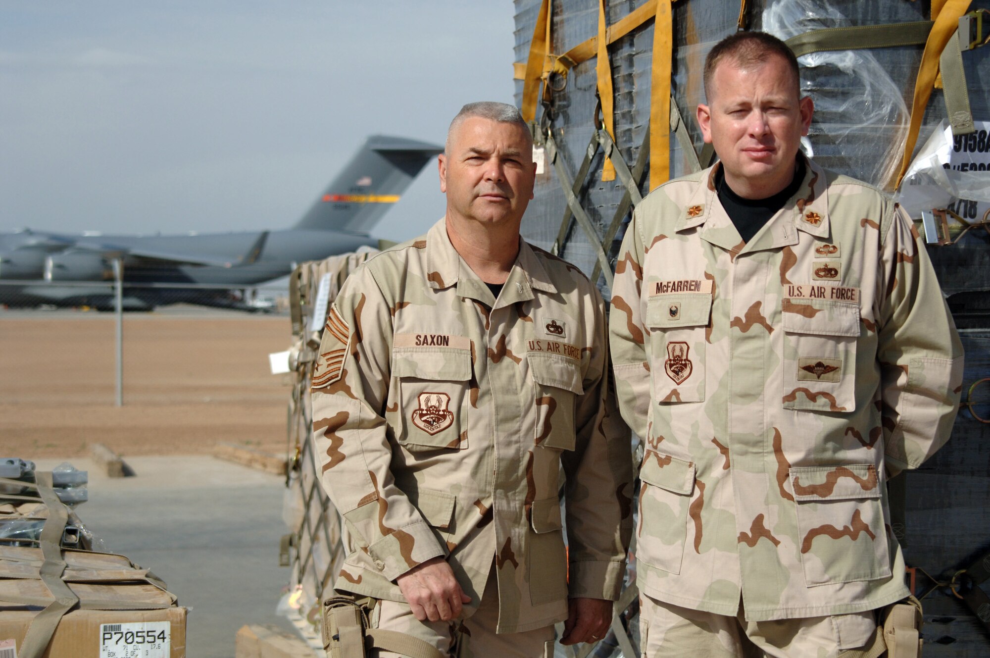 BALAD AIR BASE, Iraq -- (From right) Maj. Preston McFarren, Aerial Port Flight commander, and Chief Master Sgt. Steven Saxon, superintendent, stand next to pallets prepared for delivery to servicemembers downrange at the cargo yard at Balad Air Base, Iraq. Major McFarren and Chief Saxon are assigned to the 332nd Expeditionary Logistics Squadron with the 332nd Air Expeditionary Wing. They are deployed here together from the 443rd Airlift Wing?s 26th Aerial Port Squadron at Lackland Air Force Base, Texas. Balad Air Base is the aerial port hub for all of Iraq and the busiest cargo aerial port in the Department of Defense. (U.S. Air Force photo by Senior Airman Candace Romano)
