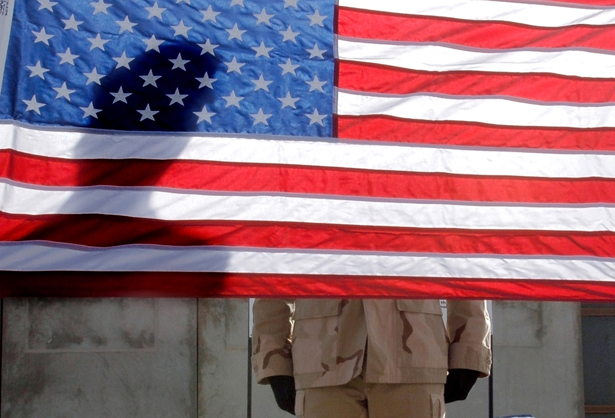 The sun cast a diagonal shadow of Staff Sgt. Jody Nitz on the U.S. flag while he and fellow Airmen conducted an official flag raising and folding ceremony April 21 in Baghdad, Iraq. The Sather Air Base Honor Guard raised and folded 23 U. S. flags. Sergeant Nitz is assigned to the 447th Expeditionary Medical Squadron. (U.S. Air Force photo/Tech. Sgt. Cecilio M. Ricardo Jr.)