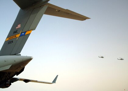 A C-17 Globemaster III from Charleston Air Force Base, S.C., is readied for cargo loading while two Marine AH-64 Cobra attack helicopters pass over April 21 at Al Asad Air Base, Iraq. Since January, Airmen from the 438th Aerial Port Flight at Al Asad have processed more than 32,000 passengers, 15,528 tons of cargo and more than 2,600 aircraft, keeping nearly 12,000 American servicemembers off the roads in convoys. (U.S. Air Force photo/Capt. Ken Hall)
