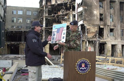Army Maj. Gen. James T. Jackson presents FBI special agent Arthur Eberhart a poster-sized photo of the American flag unfurled from the roof of the Pentagon Sept. 12, the day after terrorist crashed a hijacked jetliner into the building. Eberhart, special agent in charge of the FBI crime scene investigation at the Pentagon, turned over control of  the site to Jackson's command, the Military District of Washington, in a transfer ceremony Sept 26, 2001.