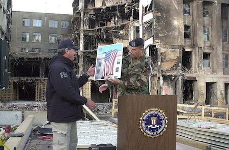 Army Maj. Gen. James T. Jackson presents FBI special agent Arthur Eberhart a poster-sized photo of the American flag unfurled from the roof of the Pentagon Sept. 12, the day after terrorist crashed a hijacked jetliner into the building. Eberhart, special agent in charge of the FBI crime scene investigation at the Pentagon, turned over control of  the site to Jackson's command, the Military District of Washington, in a transfer ceremony Sept 26, 2001.