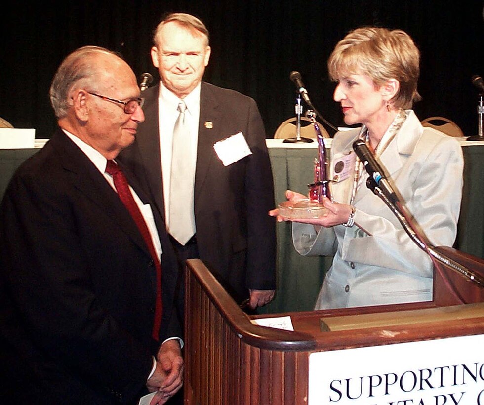Mary M. Keller (right), presents Walter Kaye a token of appreciation on behalf of the Military Child Education Coalition. Kaye and his wife were declared "platinum level patrons and special guardian angels." The award was presented during the coalition's 3rd annual conference, held in Palm Harbor, Fla., in July. Retired Army Lt. Gen. Pete Taylor, MCEC chairman, watches in the background. Photo by Rudi Williams.