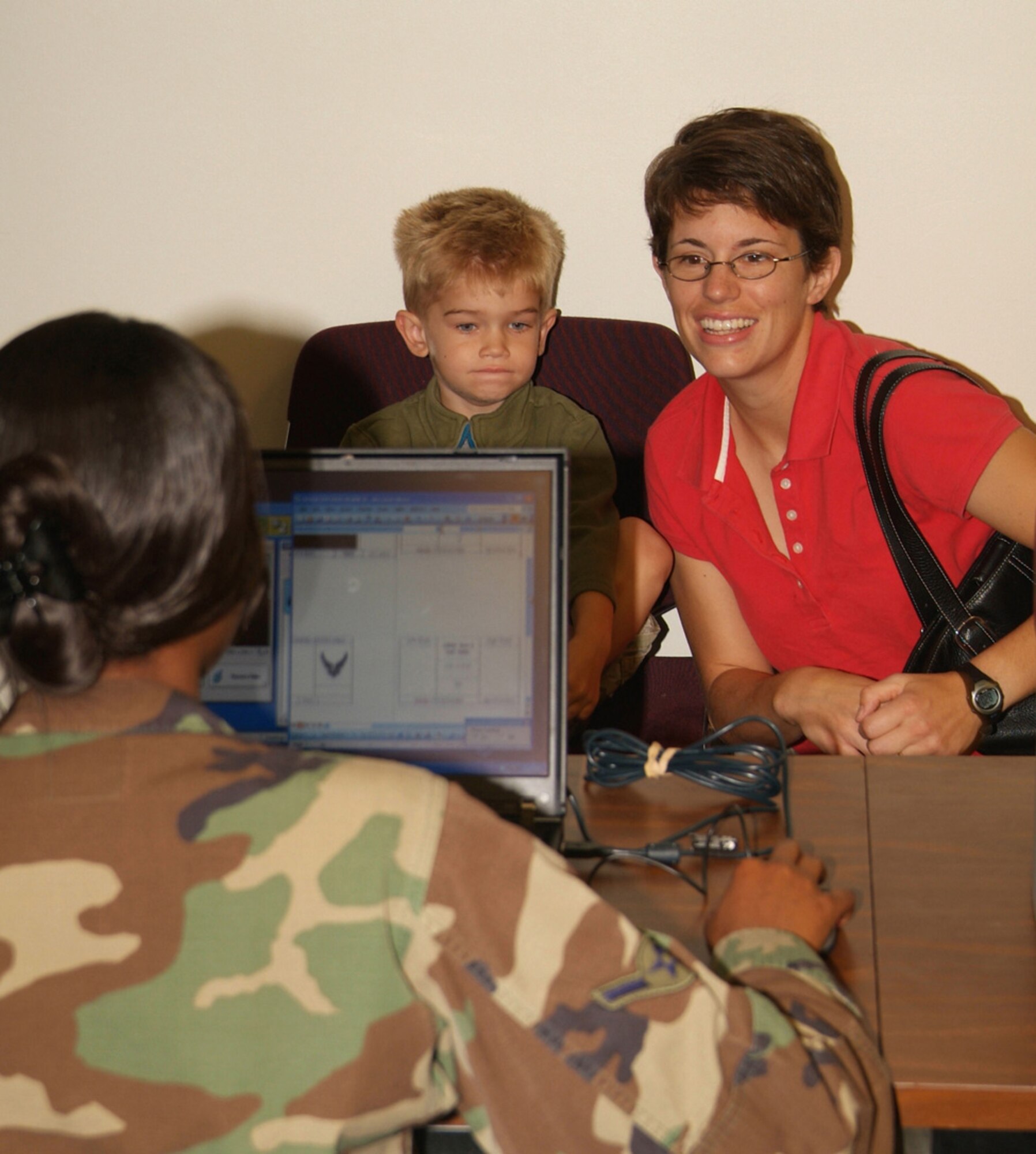 Airman Stephanie Williams, 81st Training Group, creates an identification card for 4-year-old Thomas Gorline as his mom, Gretchen, watches.  His father, Chaplain (Capt.) Jeremy Gorline, is currently deployed.  (U.S. Air Force photo by Adam Bond)