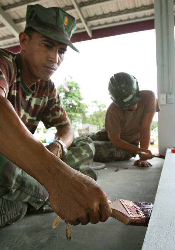 Chief Petty Officer 1st Class Pallop Naewwab, Thai Marines Engineer Battalion and Seaman Kathryn R. Henderson, builder, NMCB-3, paint the trim on the stage of the new multipurpose room built by both services for Wat Nong Grab Elementary School May 9.