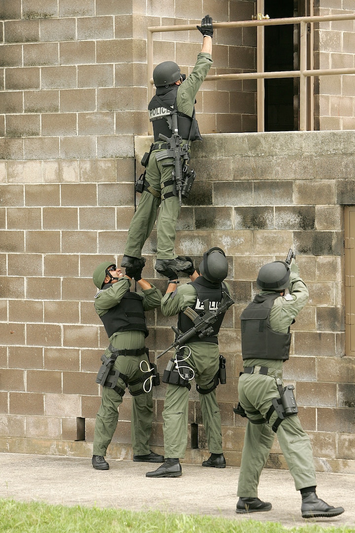 Members of the 37th Training Wing's Emergency Services Team use a team lift technique to enter a target building during training May 4 at Lackland Air Force Base, Texas. A five-man team consisting of 1st Lt. Stephen Addington, Senior Master Sgt. Matt Harmatuk, Tech. Sgt. Jason Attinger, Tech. Sgt. Justin King and Senior Airman Andrew Caro competed in the Southeast Texas SWAT Competition April 24 in Beaumont, Texas. Lackland AFB's team took a first place in the competition. (U.S. Air Force photo/Robbin Cresswell)