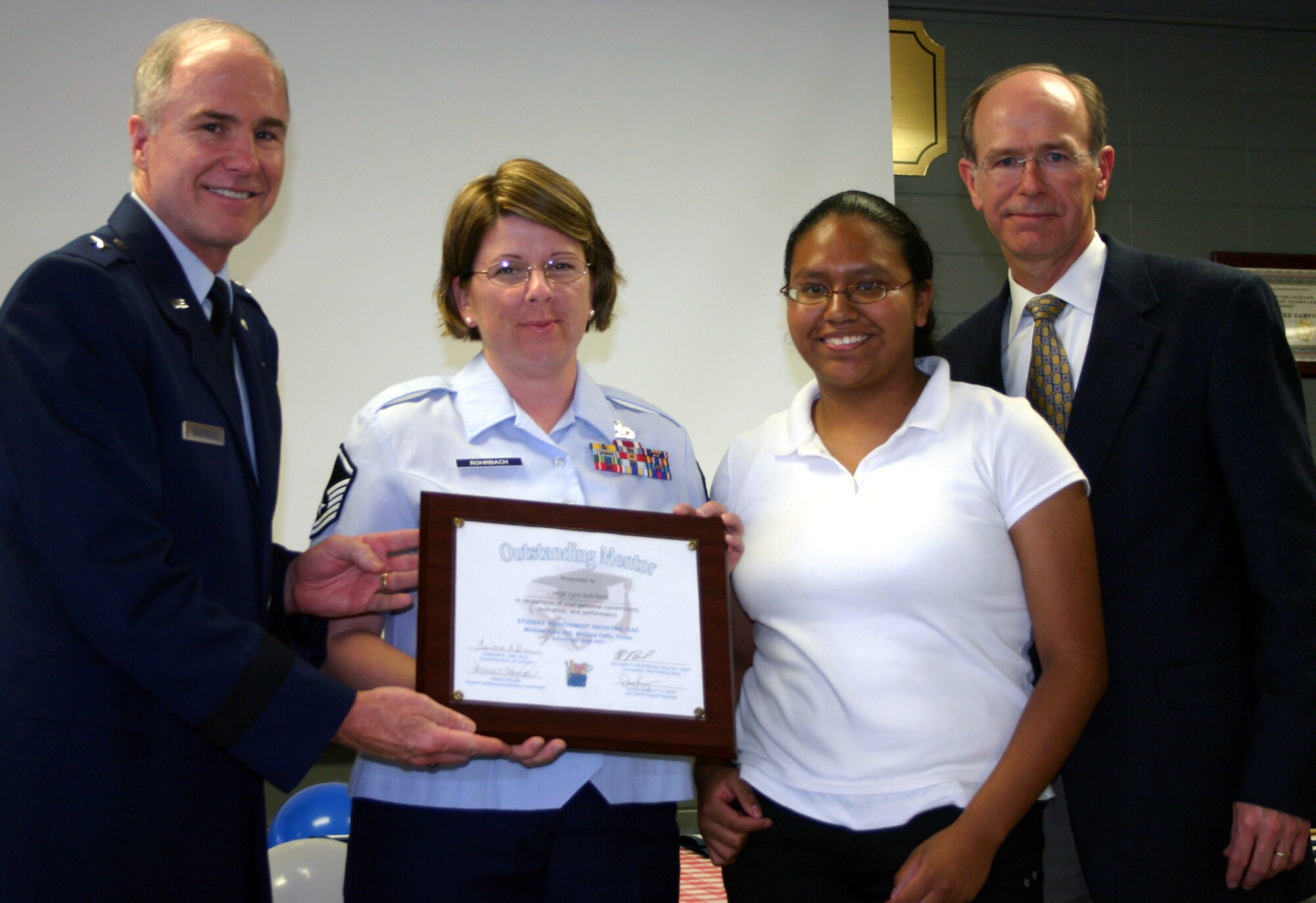 82nd Training Wing Commander Brig. Gen. Richard Devereaux and Wichita Falls Independent School District superintendent Dr. Dawson Orr present an Outstanding Mentor plaque to Master Sgt. Lynn Rohrbach, 365th Training Squadron, in a ceremony at Washington-Jackson Elementary School May 10. Sergeant Rohrbach serves in the Student Achievement Initiative as a mentor to Zundy Junior High School student Aidee Rubio, also pictured. (U.S. Air Force photo/Staff Sgt. Tonnette Thompson)