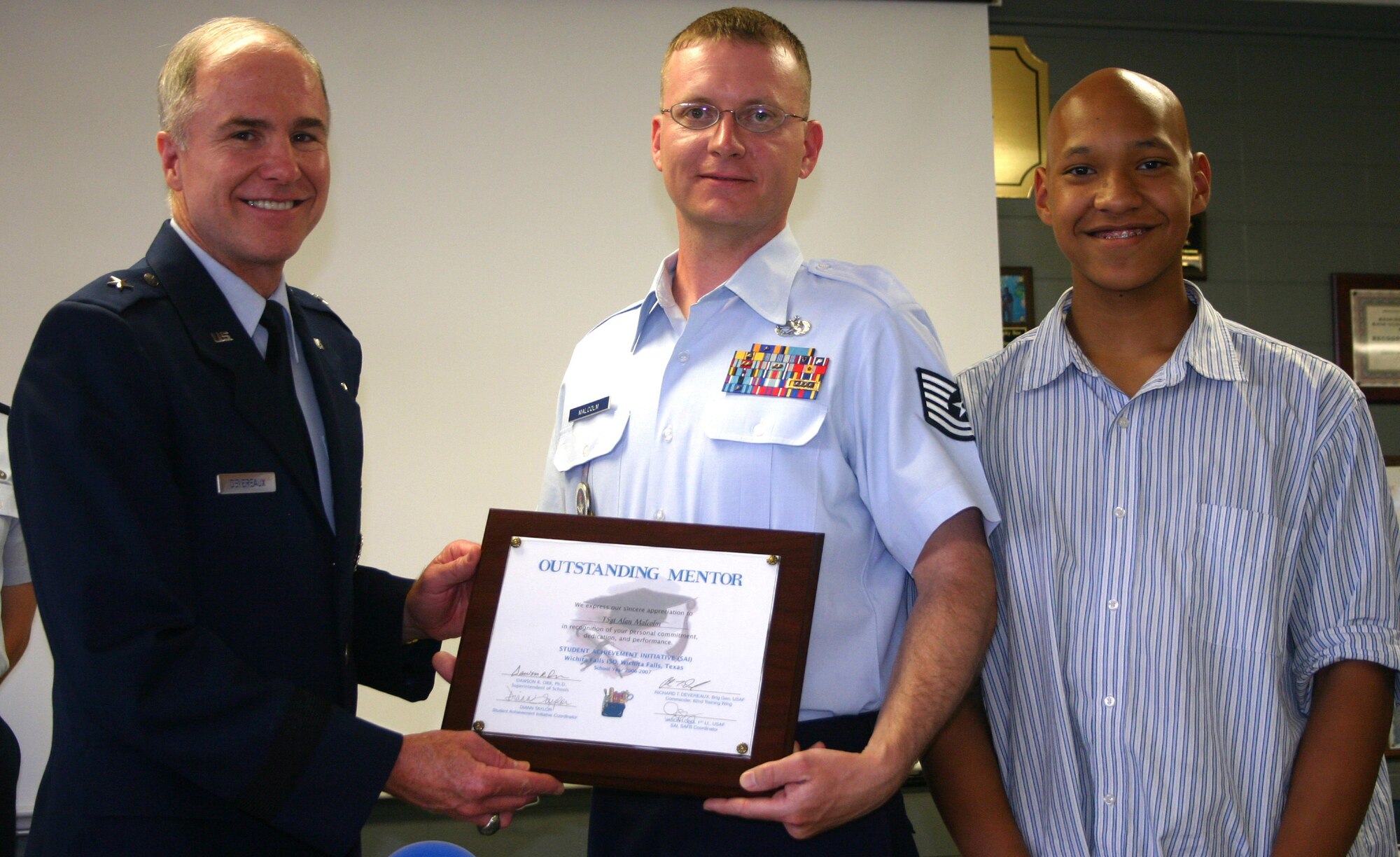 82nd Training Wing Commander Brig. Gen. Richard Devereaux presents an Outstanding Mentor plaque to Tech. Sgt. Alan Malcolm, 360th Training Squadron, in a ceremony at Washington-Jackson Elementary School May 10. Sergeant Malcolm serves in the Student Achievement Initative as a mentor to McNiel Junior High School student Avery Heanu, right. (U.S. Air Force photo/Staff Sgt. Tonnette Thompson)