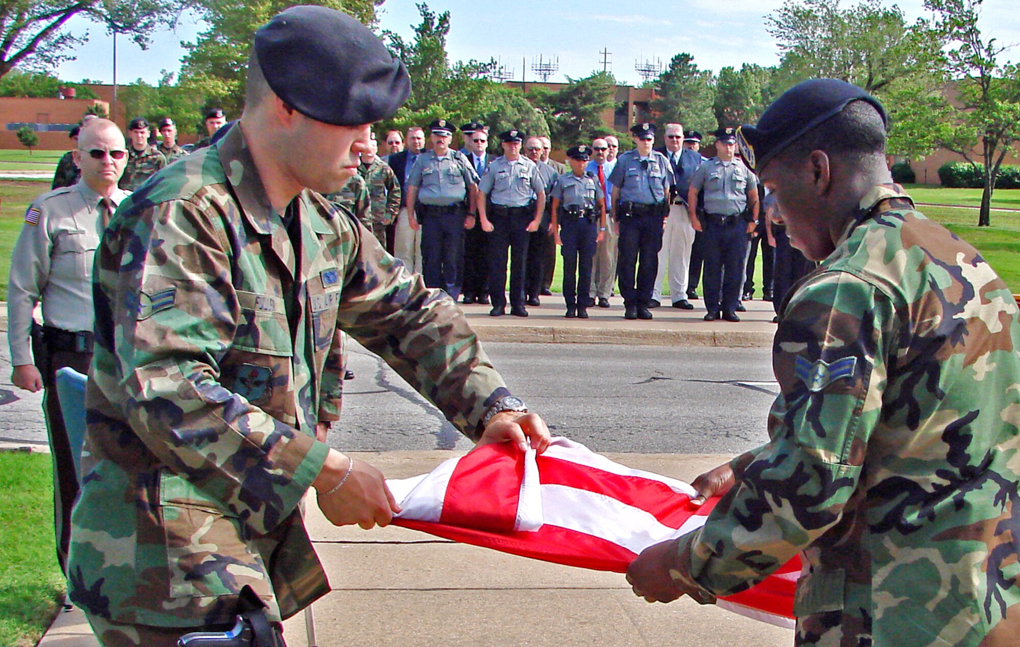 Airmen 1st Class Daniel Fuller and Damon Beasley, 71st Security Forces Squadron, fold the flag during the National Peace Officers Memorial Day formal retreat at Vance Air Force Base Tuesday. Garfield County (Okla.) Sheriff Bill Winchester, far left, was guest speaker for the ceremony. The flight in the background was formed by representatives of local law enforcement agencies. May 15 has been National Peace Officers Memorial Day, and the week containing May 15 has been National Police Week, since President John Kennedy signed Public Law 87-726 on Oct.1, 1962.  (U.S. Air Force photo by Frank McIntyre)  