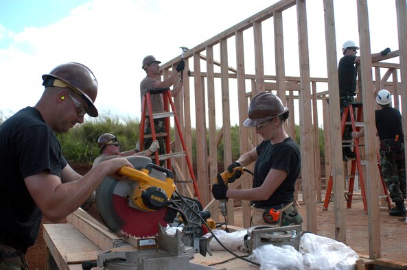 301st Civil Engineer Squadron members Staff Sgt. Jeremy Glenn (left) and Staff Sgt. Krista Kenoyer cut boards as (from left) Senior Airman Doug Weir, Senior Airman Robert Wolf, Senior Master Sgt. Skip Kiefhaber and Senior Airman Matthew Ducckett work to fram a house as parto fo a project to bui8ld housing for the elderly and handicapped next to Helemano Plantantion on Oahu, Hawaii. (U.S. Air Force Photo/Tech. Sgt. Stephen Bailey)