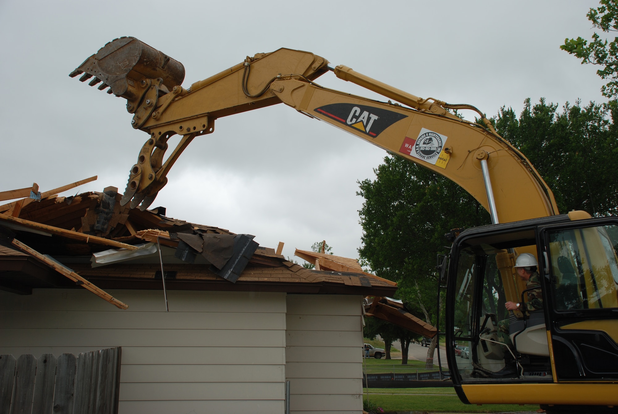 Brig. Gen. Richard Devereaux, behind the controls of an excavator, demolishes a Wherry housing home at the site of new officer and senior enlisted homes May 15. (U.S. Air Force photo/Airman 1st Class Jacob Corbin)